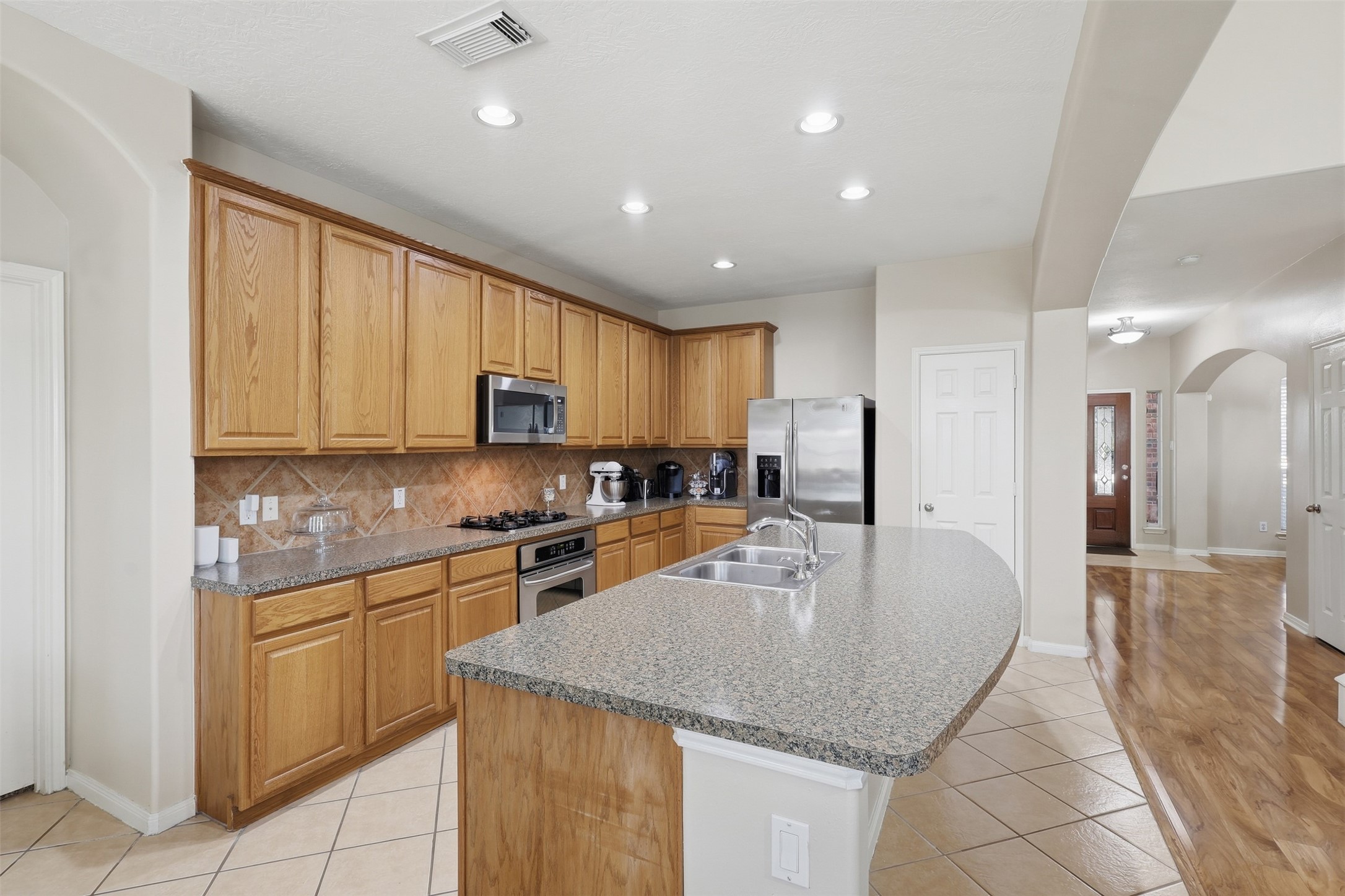 Beautifully appointed kitchen features abundant tall cabinetry, tile backsplash, built-in stainless-steel appliances, and a massive center island with generous workspace. The open design provides a seamless connection to the family room and breakfast area. Wait till you see the walk-in pantry!  Make that call!