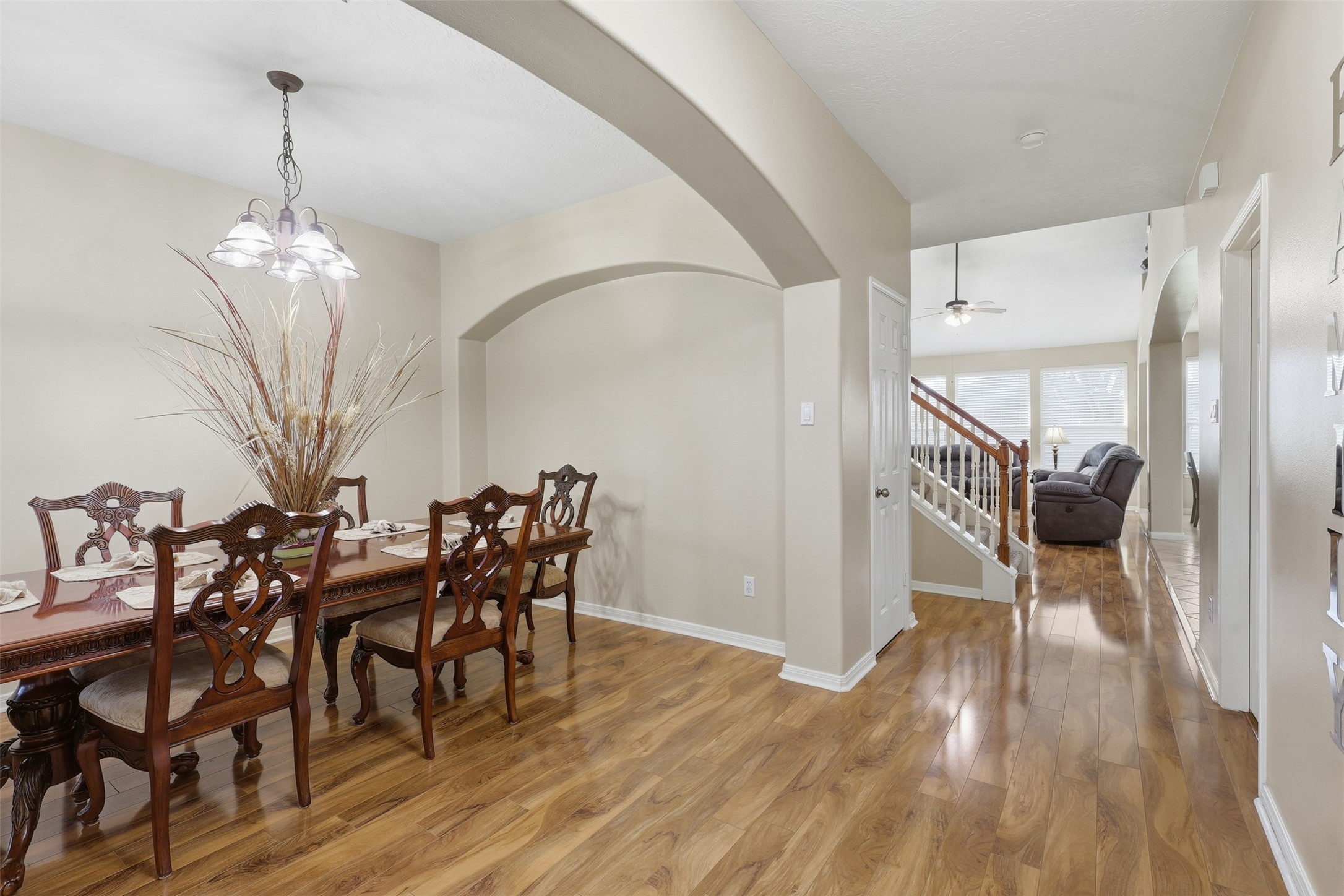 Step inside to an inviting formal dining room featuring rich wood-look flooring, elegant arched openings, soaring ceilings, and a beautiful chandelier. The open design creates a graceful setting for holiday dinners, celebrations, and memorable gatherings.