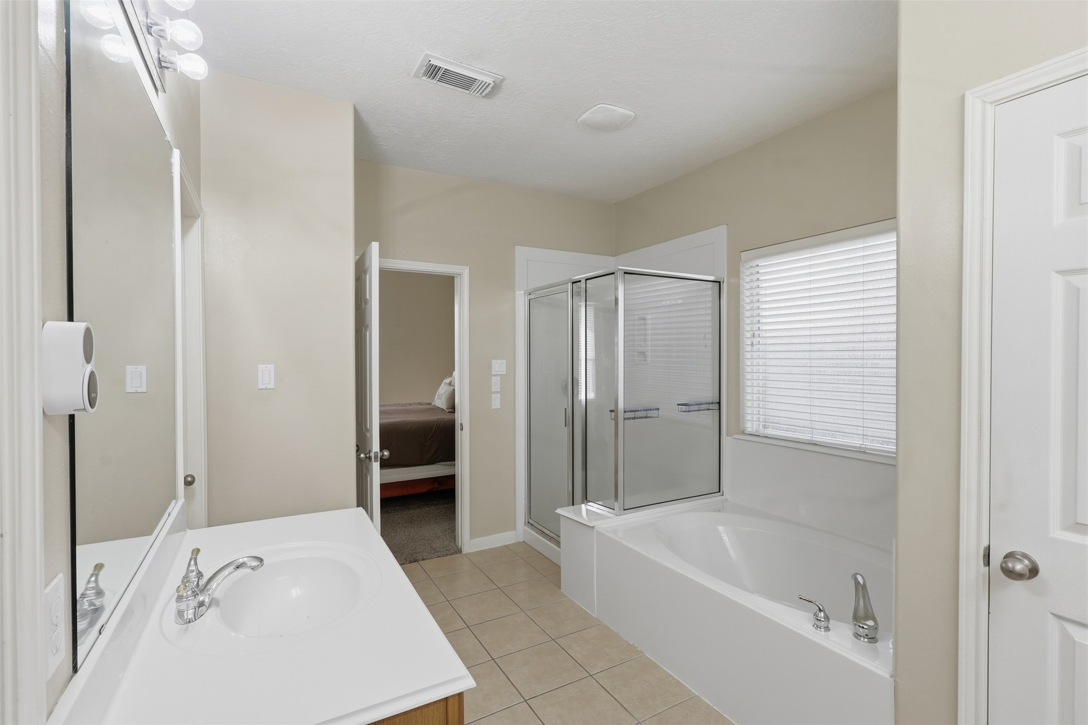 Another view of the spacious primary bath highlights the dual vanity, generous counter space, soaking tub, and separate walk-in shower. Neutral finishes and natural light create a bright, relaxing atmosphere.