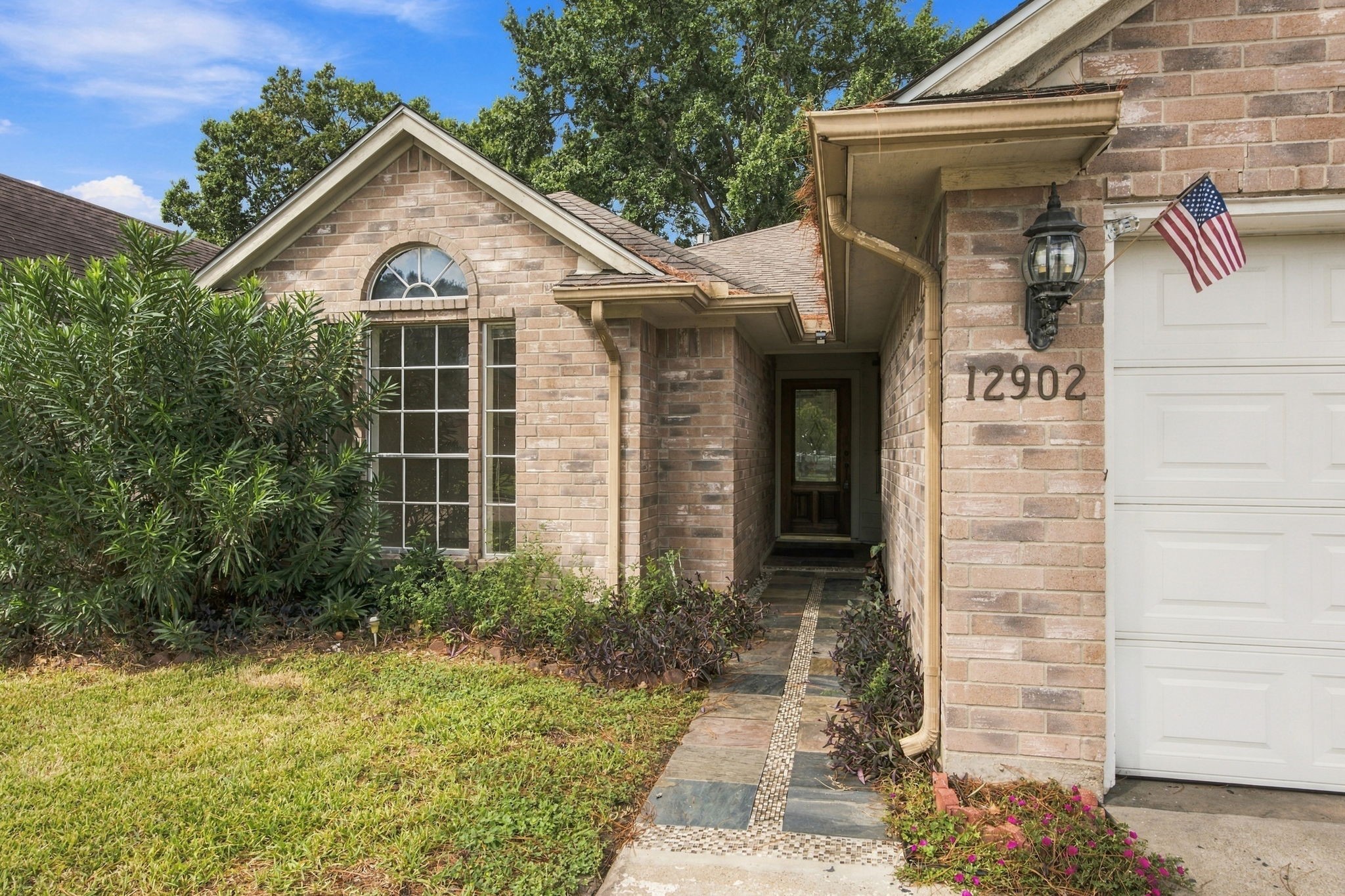 A tiled walkway leads to the recessed entry, with an arched front window adding architectural charm.