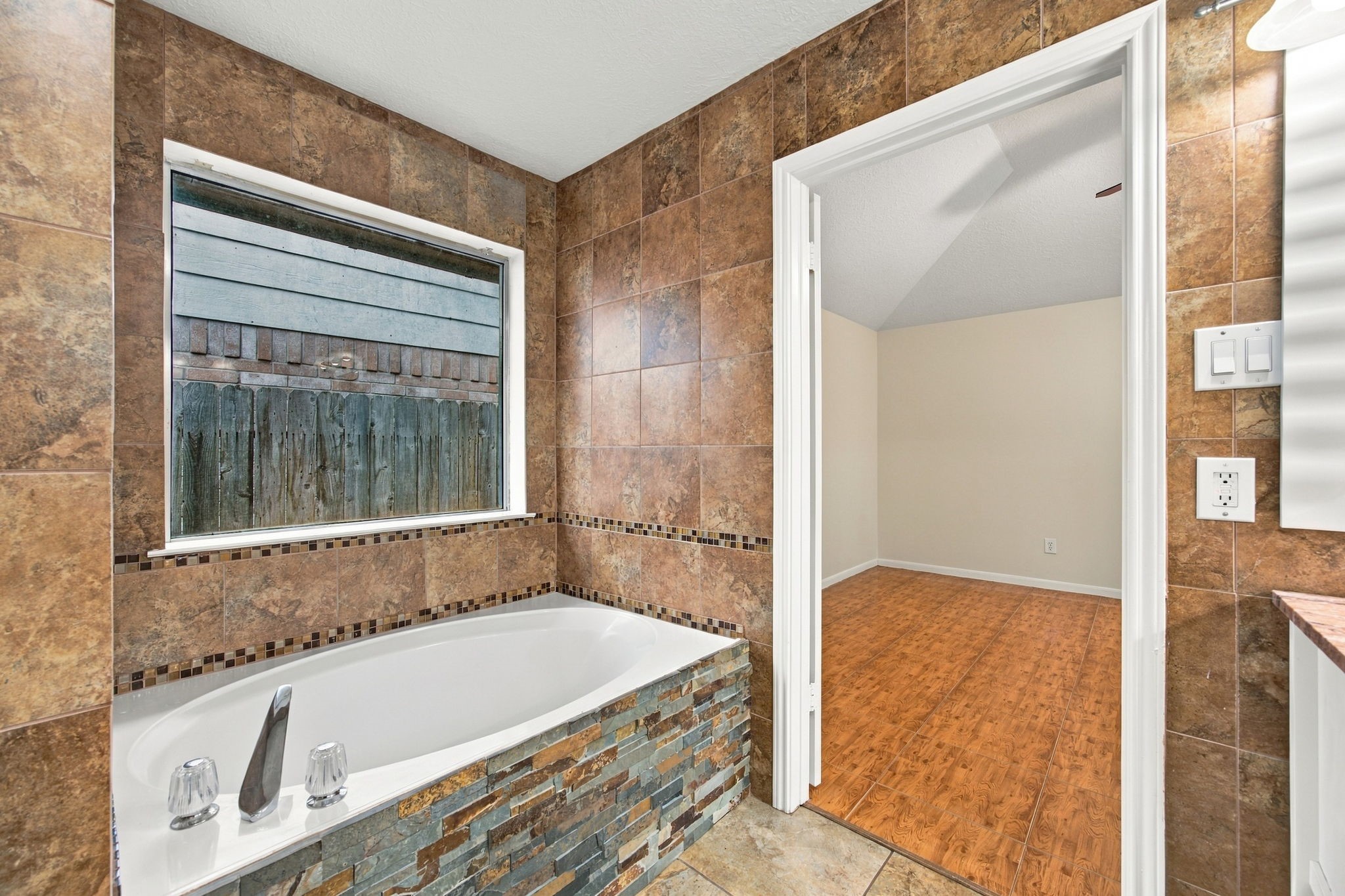 Positioned beneath a window, the soaking tub features a stacked-stone surround and decorative tile accents.