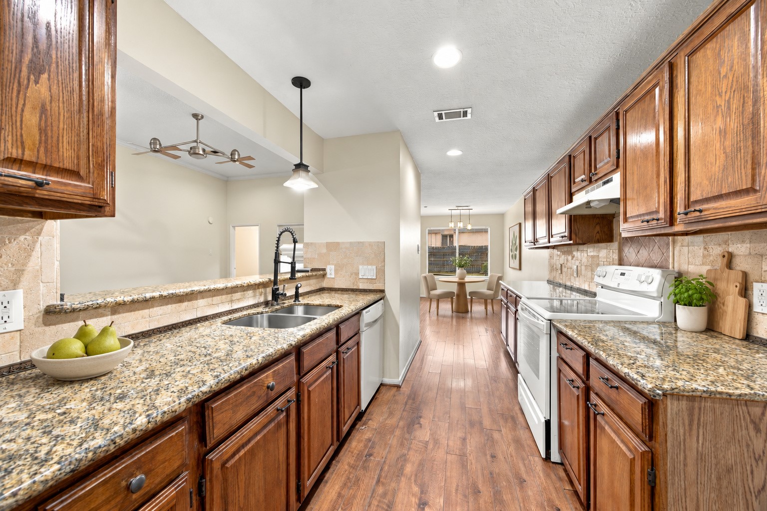 The kitchen features wood cabinetry, granite countertops, a tile backsplash, and a sink overlooking the living area. Virtually staged