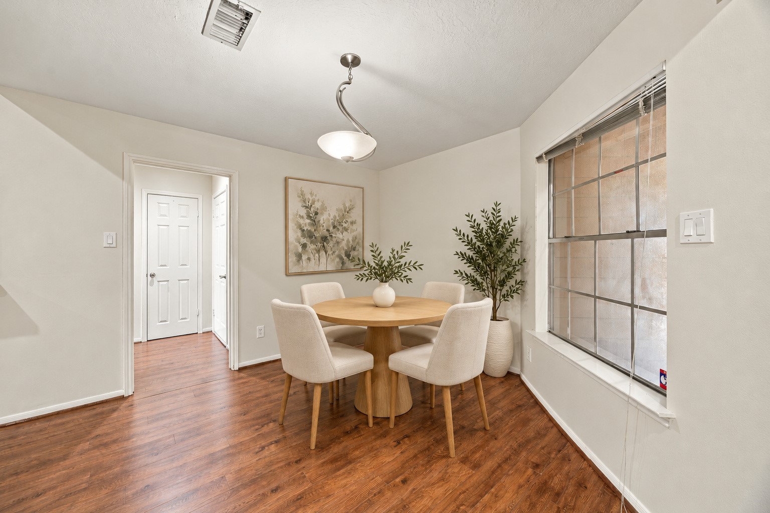 A front-facing window and overhead light define a comfortable spot for a dining table.Virtually staged