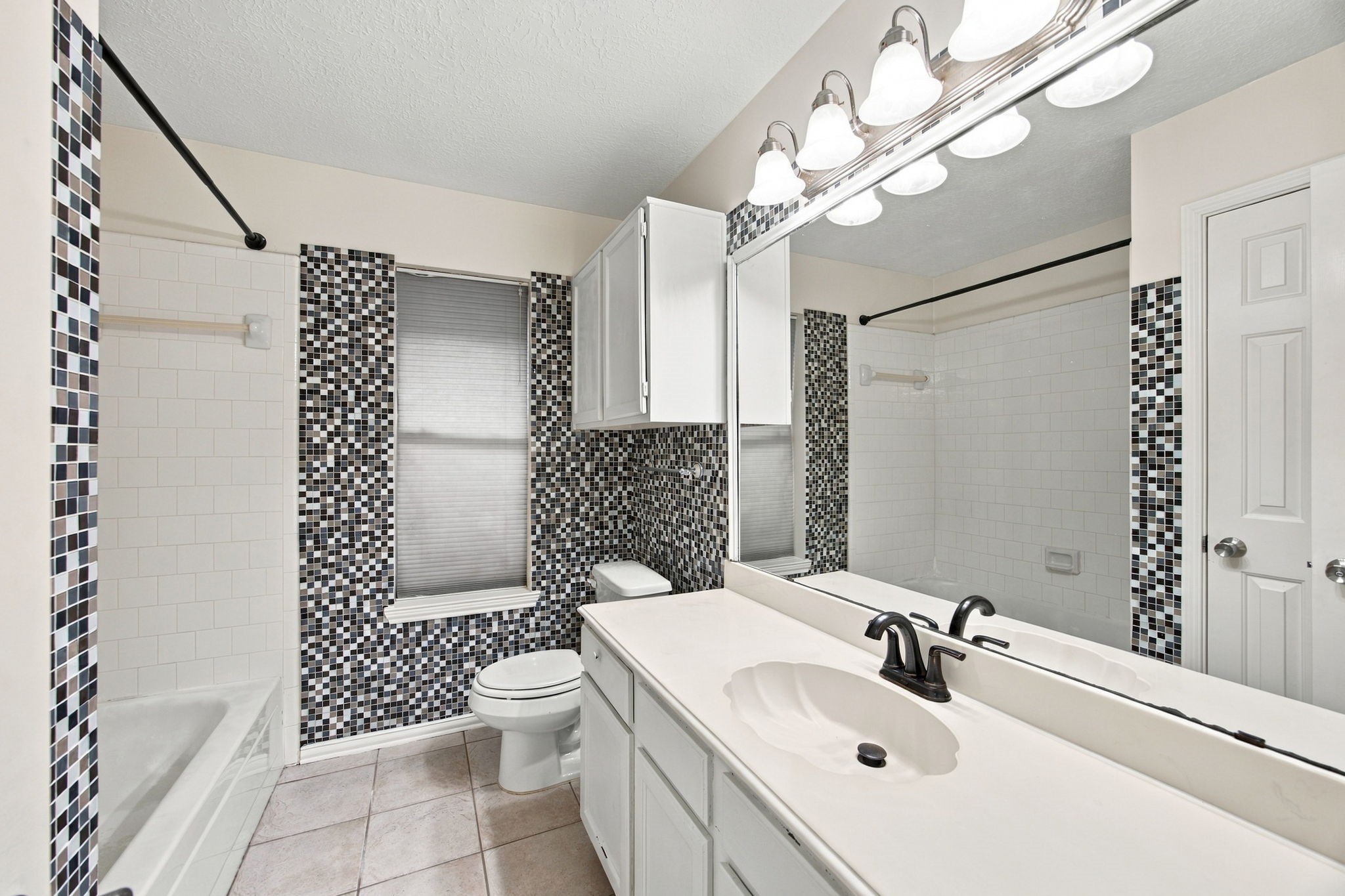 Mosaic tile accents add character to this bathroom, featuring a wide vanity, a large mirror, and a tub/shower combination.