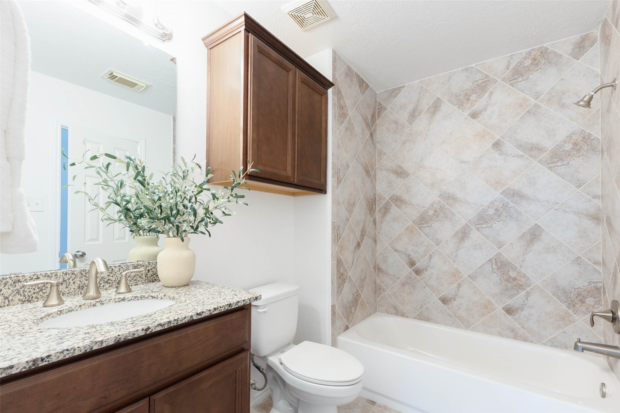 This well-appointed secondary bathroom features a generous granite-topped vanity with rich wood cabinetry offering ample storage. An oversized mirror & attractive overhead lighting complement the warm finishes, while a tub/shower combo completes the inviting, functional design.