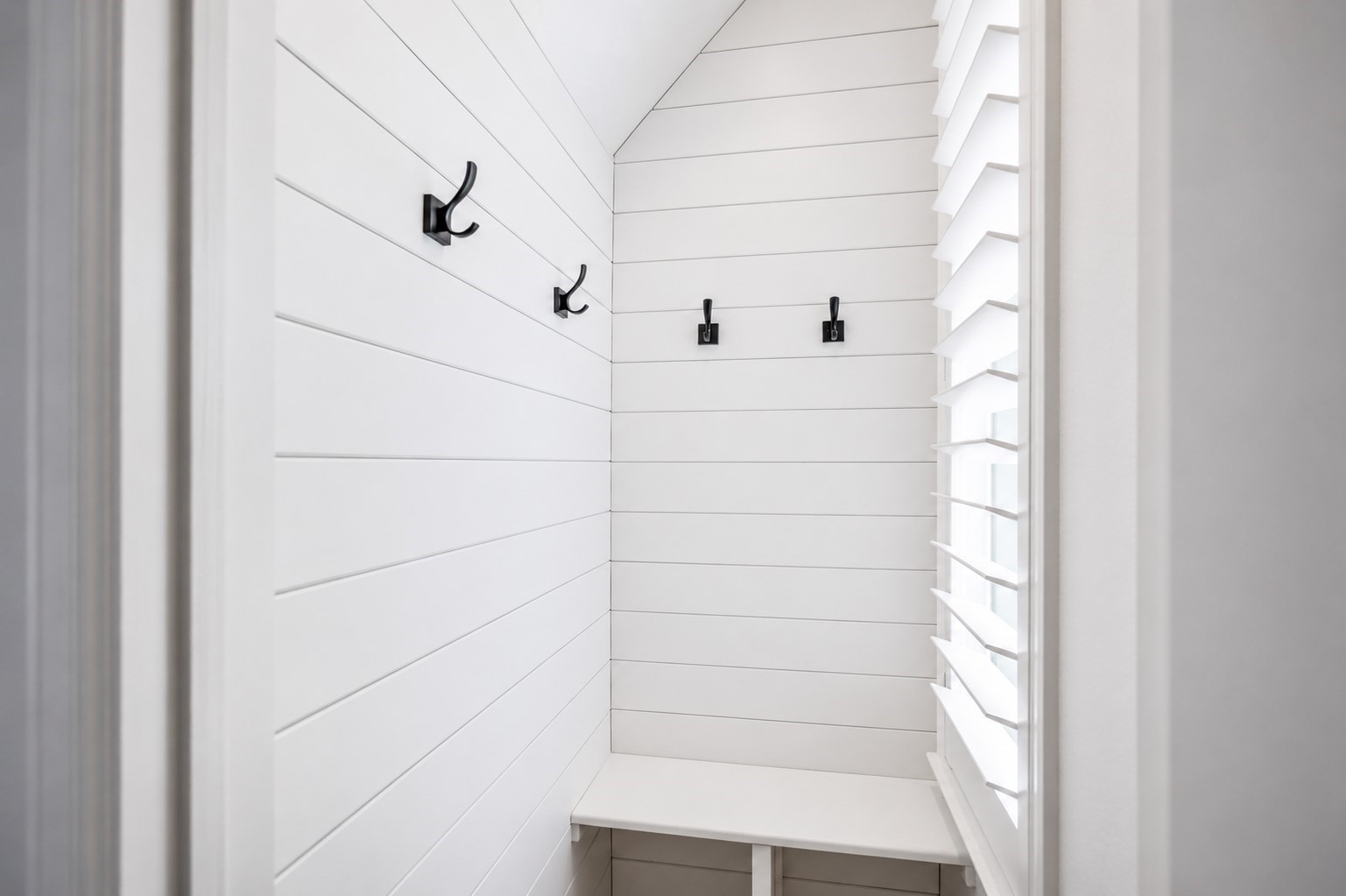 Close to the entry is a mudroom glowing with natural light, with white shiplap walls and a bench.