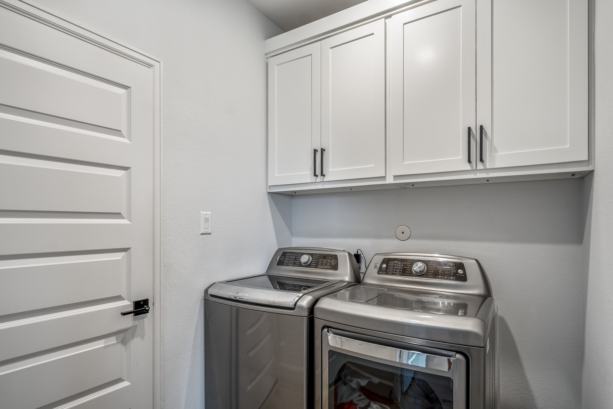 This laundry room features sleek white cabinets for storage and a clean, minimalistic design.