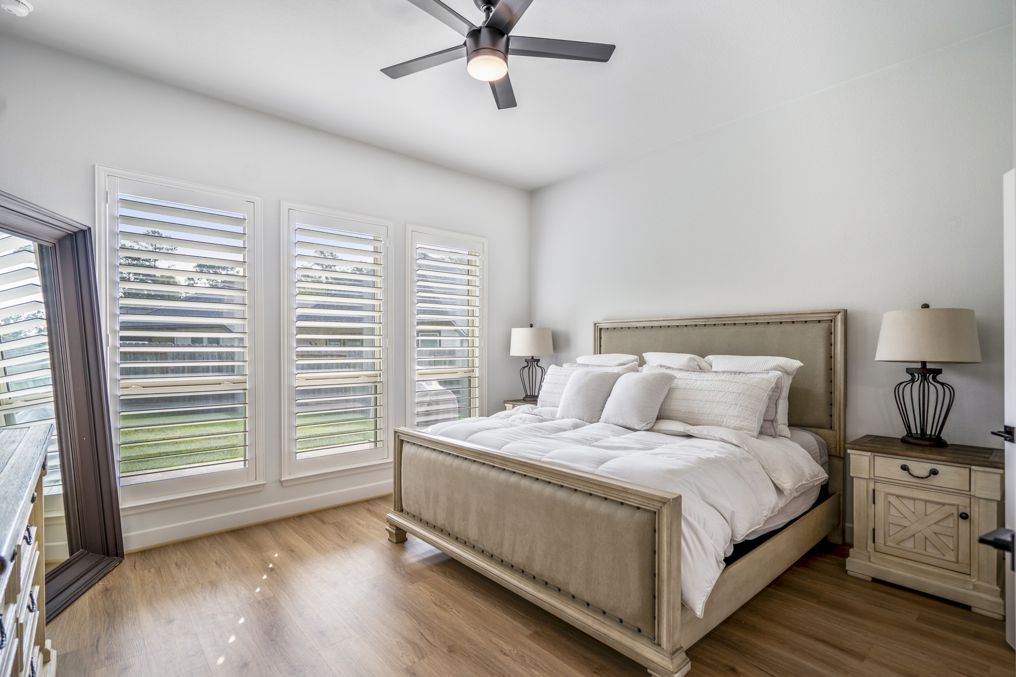 This first-floor primary suite features large windows with plantation shutters, allowing natural light to fill the space. Take note of those beautiful, upgraded floors that continue throughout.