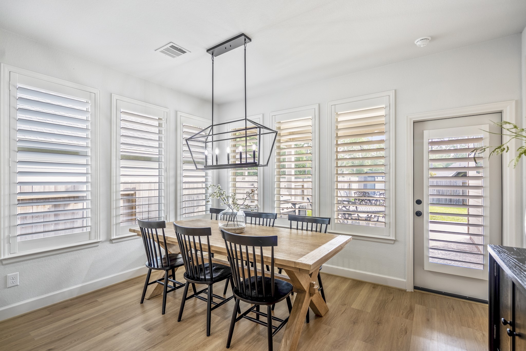 Overlooking the extended patio and generously sized lot, this breakfast space adorned with the contemporary light fixture is surrounded by a wall of windows, offering a peaceful feel.