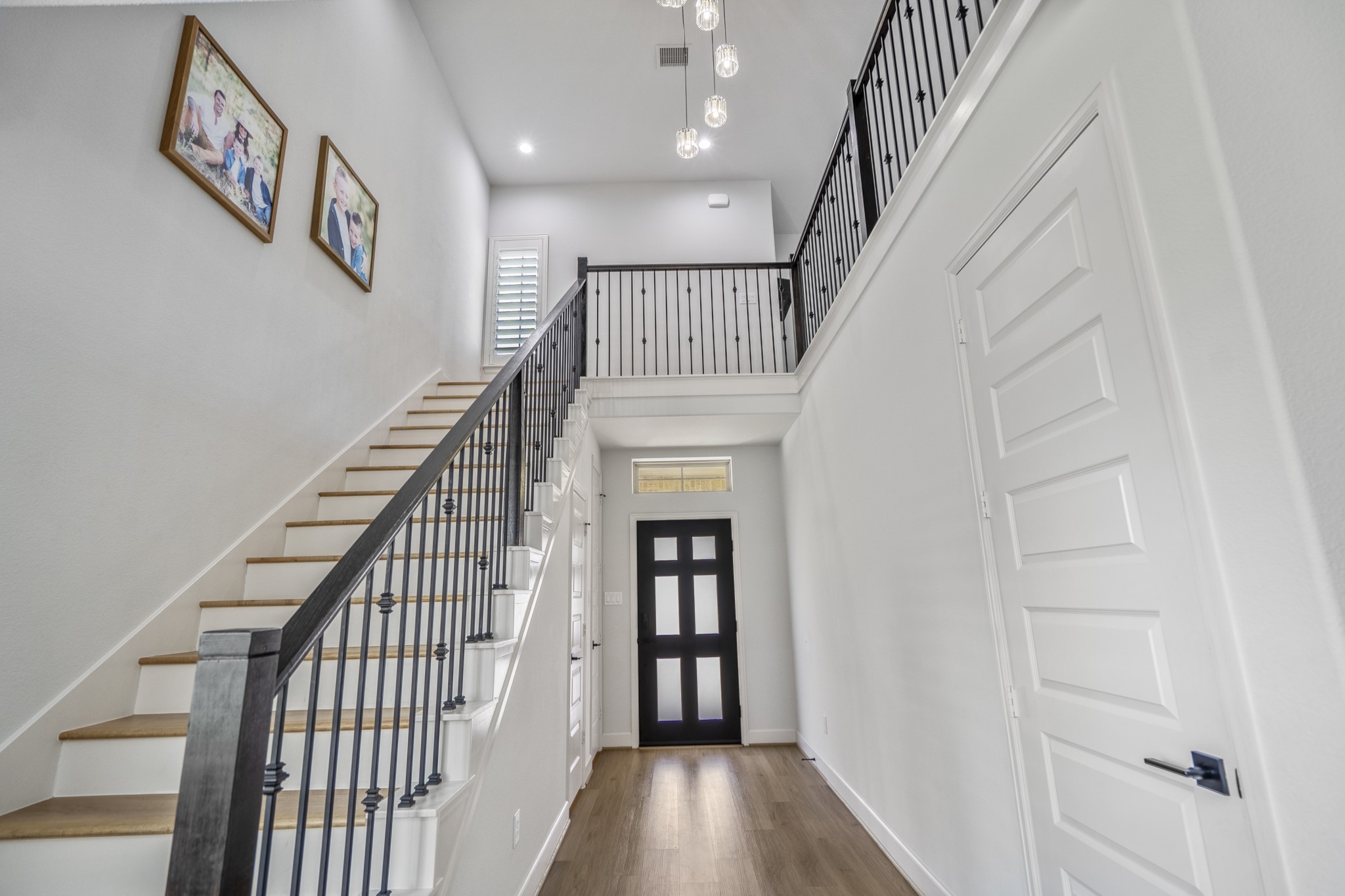 This entryway showcases a bright, modern look with a high ceiling, elegant staircase with an upgraded black railing. The space is accented by LVP flooring and contemporary light fixtures, creating a welcoming and stylish first impression.