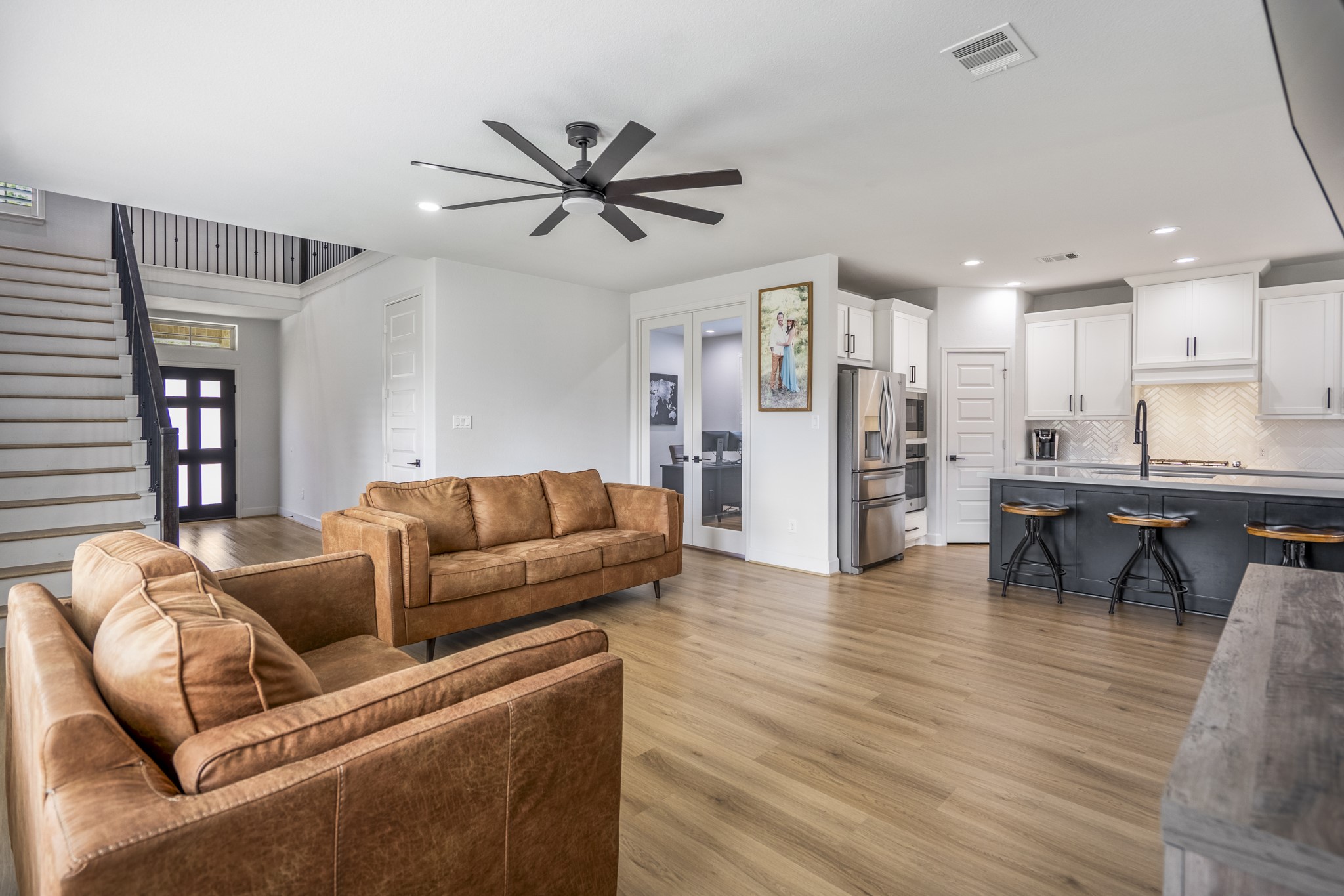 This modern open-concept living area features sleek LVP floors, a stylish kitchen with white cabinets and stainless-steel appliances, and a cozy seating area. The space is bright, with a contemporary feel.