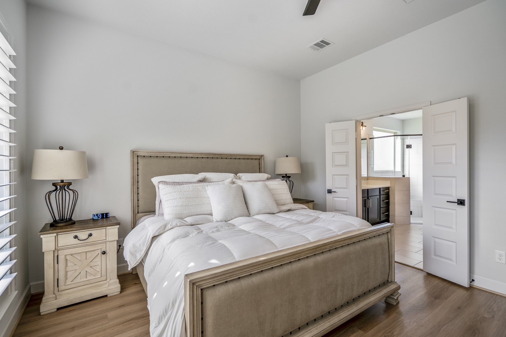 The primary bedroom boasts large windows allowing natural light to fill the space, and an en-suite bathroom beyond the double doors.