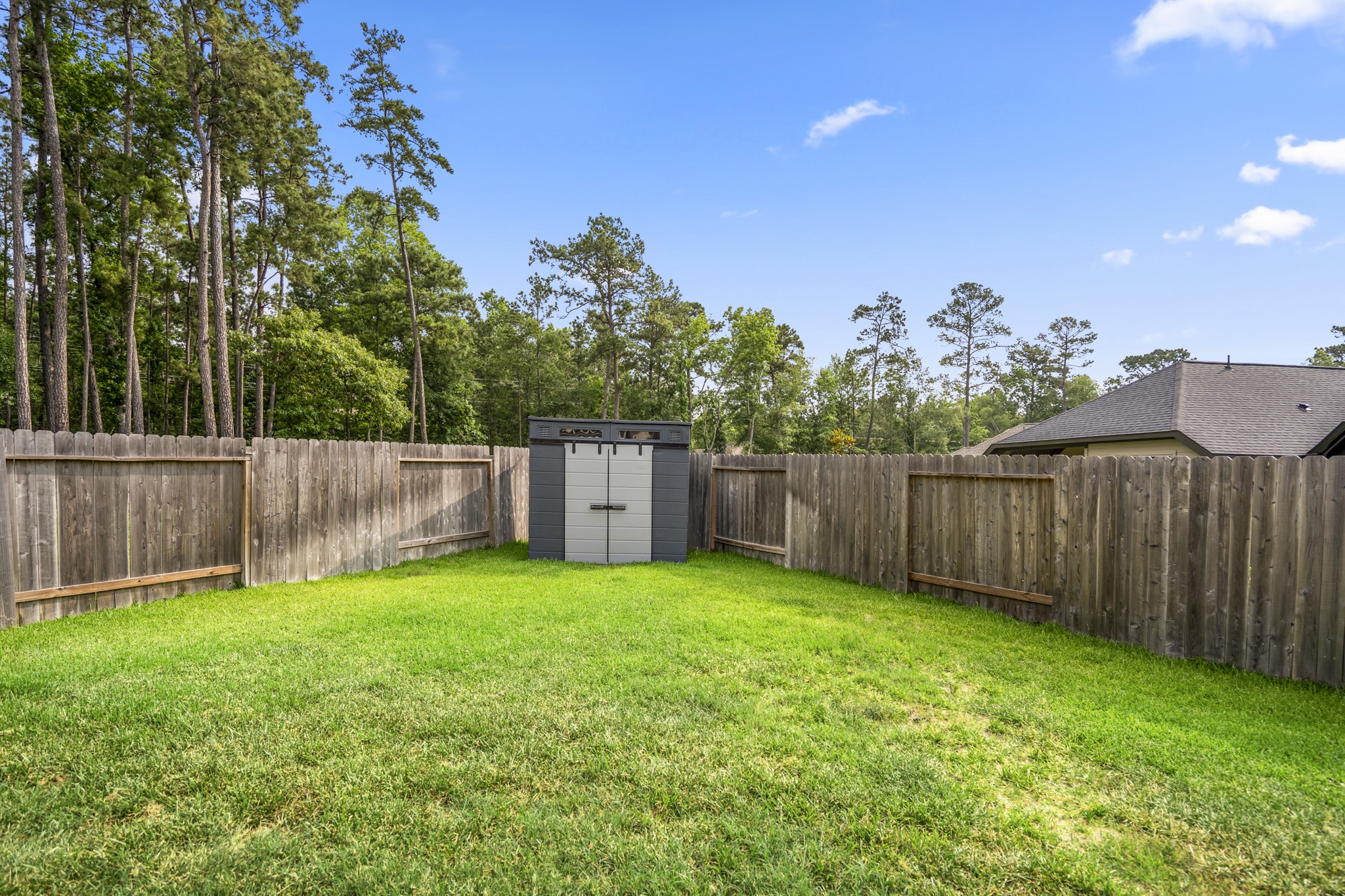 Spacious backyard featuring a well-maintained lawn, wooden privacy fence, and a storage shed, with a backdrop of tall trees. Ideal for outdoor activities and storage.