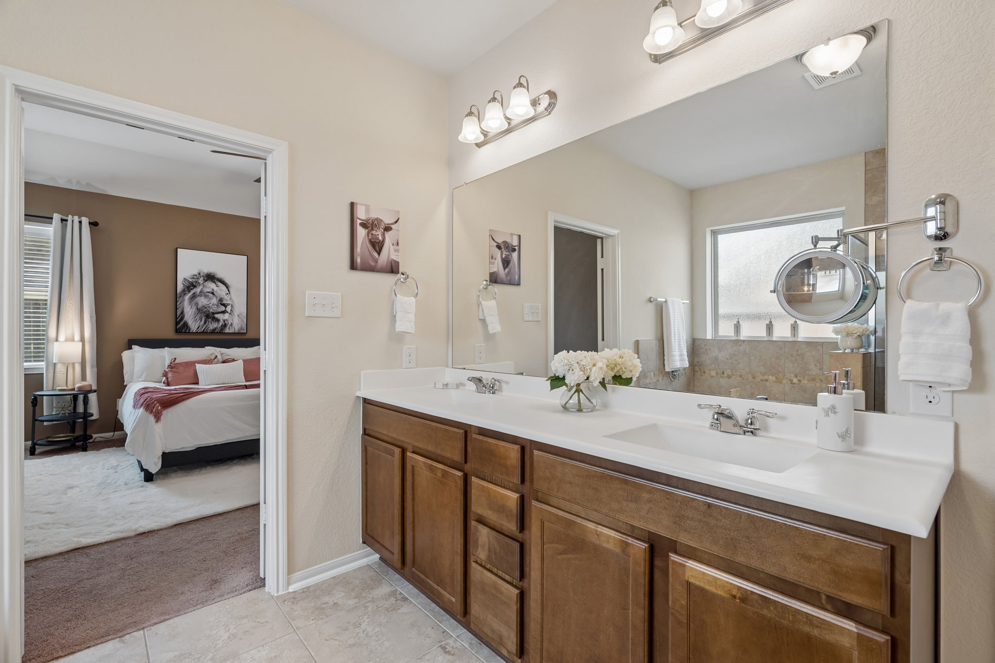 The primary bathroom features an extended dual-sink vanity with generous countertop space, warm wood cabinetry and a large wall-to-wall mirror