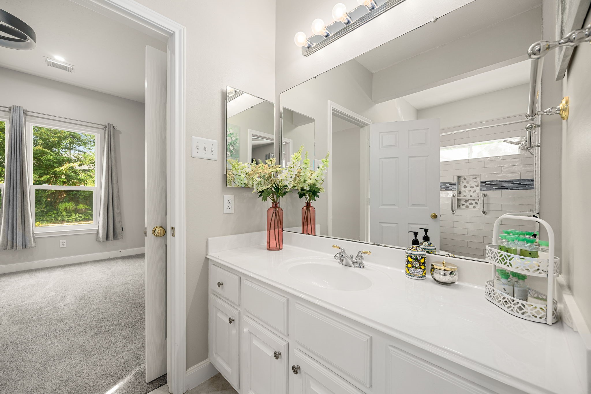 This space features a long white vanity with exceptional counter space, a large mirrored grooming area, and bright vanity lighting. Conveniently situated adjacent to a spacious secondary bedroom, this layout offers excellent functionality for children or overnight guests.