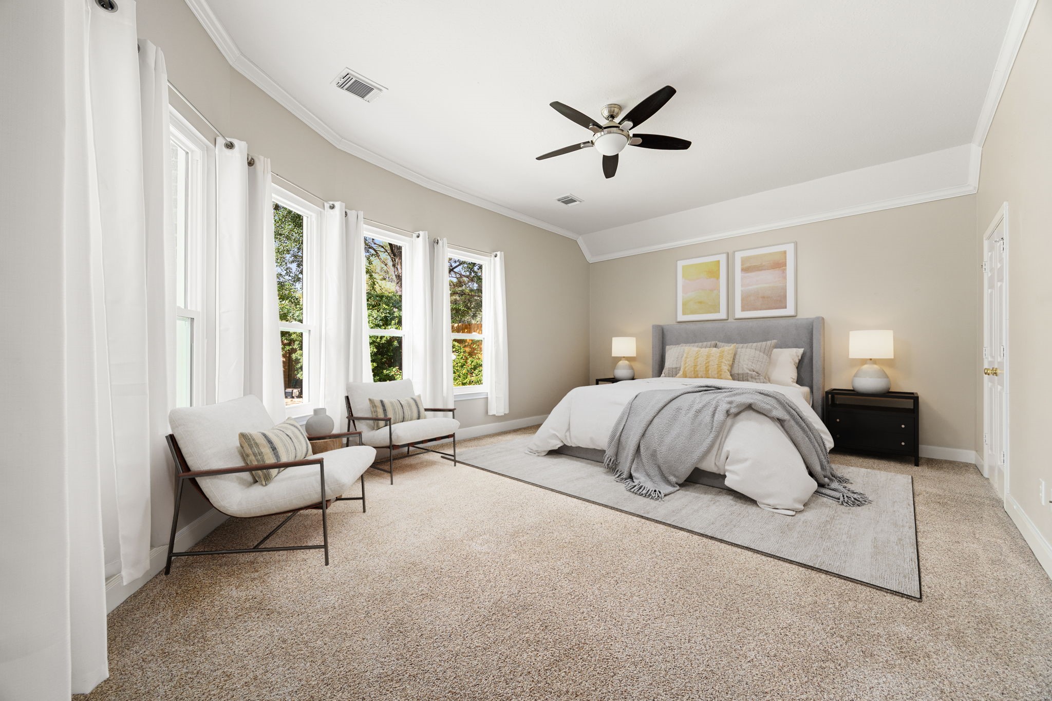 This sprawling bedroom features a striking curved wall of large bay windows that pour in beautiful natural light. Complete with elegant tray ceilings, a modern ceiling fan, and ample space for a cozy reading nook or sitting area, it offers a peaceful, spa-like escape at the end of the day.