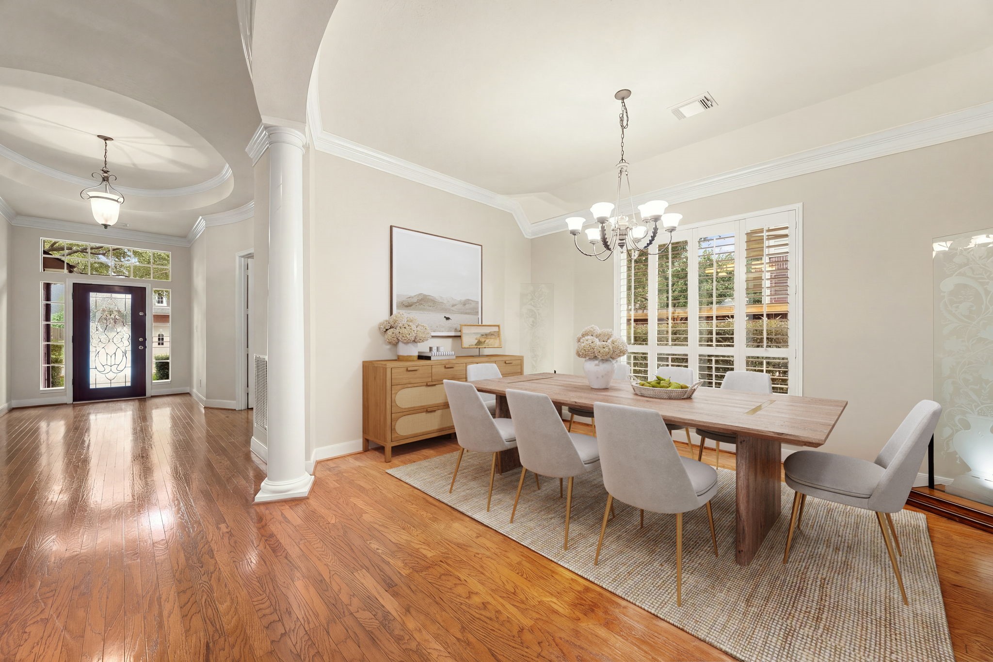 Located just off the grand rotunda entry, this sophisticated space features classic crown molding, an upscale modern chandelier, and rich hardwood flooring that flows beautifully through the open layout. Expansive windows fitted with timeless plantation shutters flood the room with natural light, creating an upscale yet welcoming atmosphere for dinner parties and holiday gatherings.