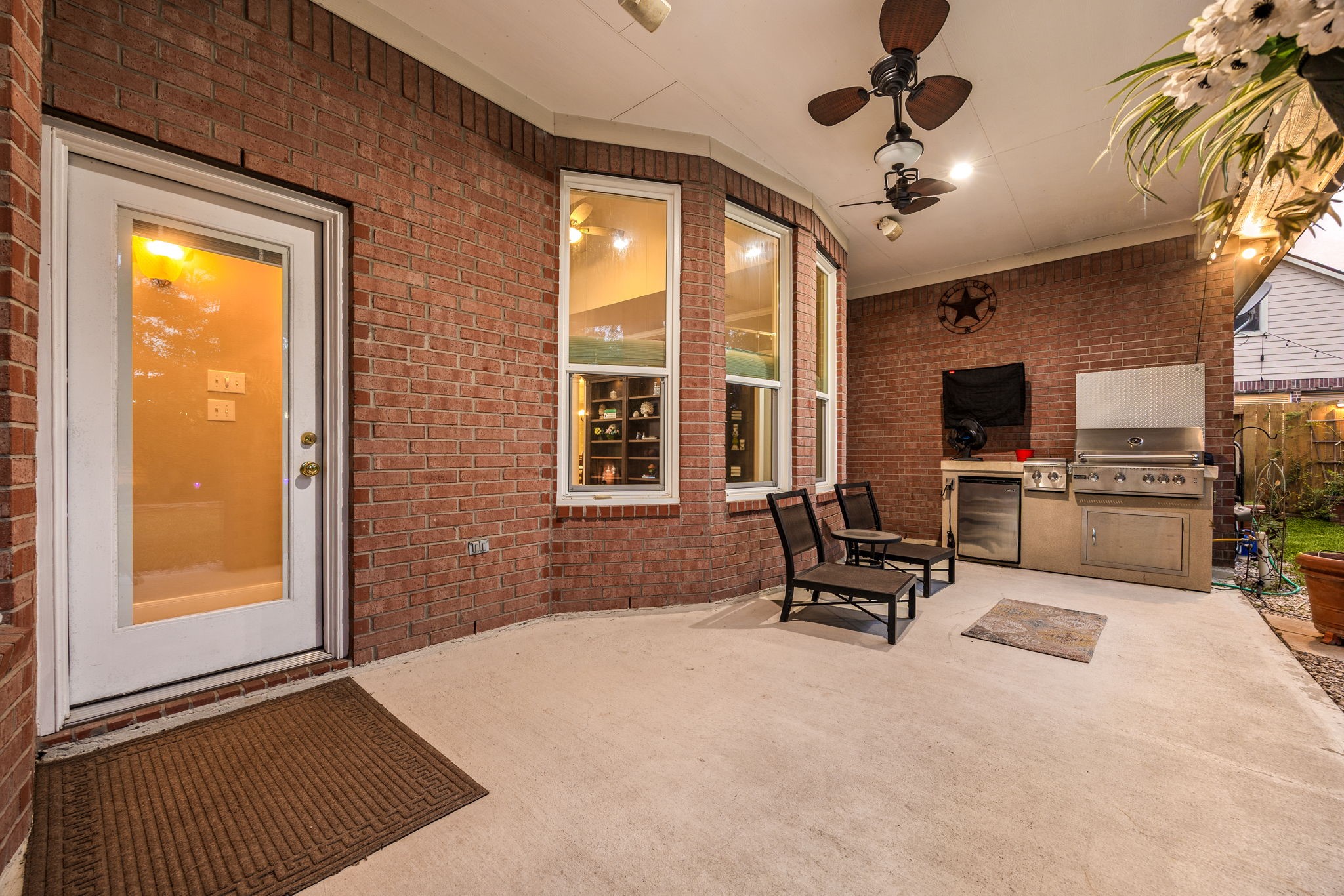 This impressive covered patio functions as a true extension of the home, featuring dual ceiling fans, a mounted television, and a premium built-in outdoor kitchen with a gas grill and mini-fridge. Surrounded by classic brick architecture and looking out to a spacious backyard, it is the absolute perfect setting for weekend barbecues and game-day entertaining.