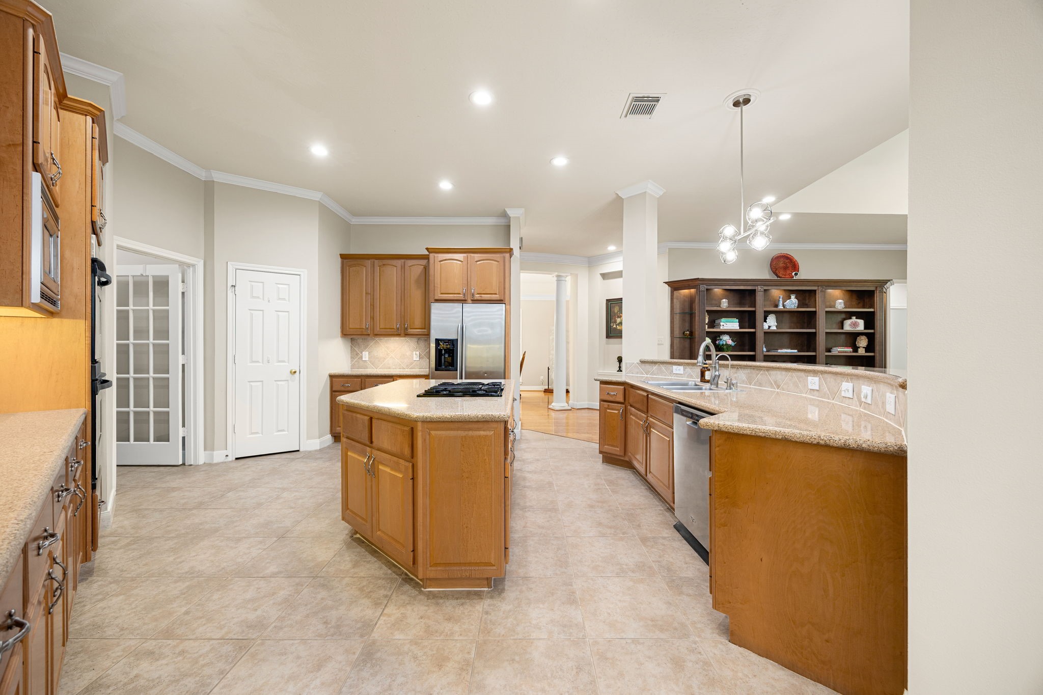 This reverse angle highlights the massive walk-in pantry hidden behind elegant French doors, a built-in workspace desk, and an expansive breakfast bar with a built-in sink and dishwasher. Every detail is optimized for convenience, organization, and effortless entertaining!
