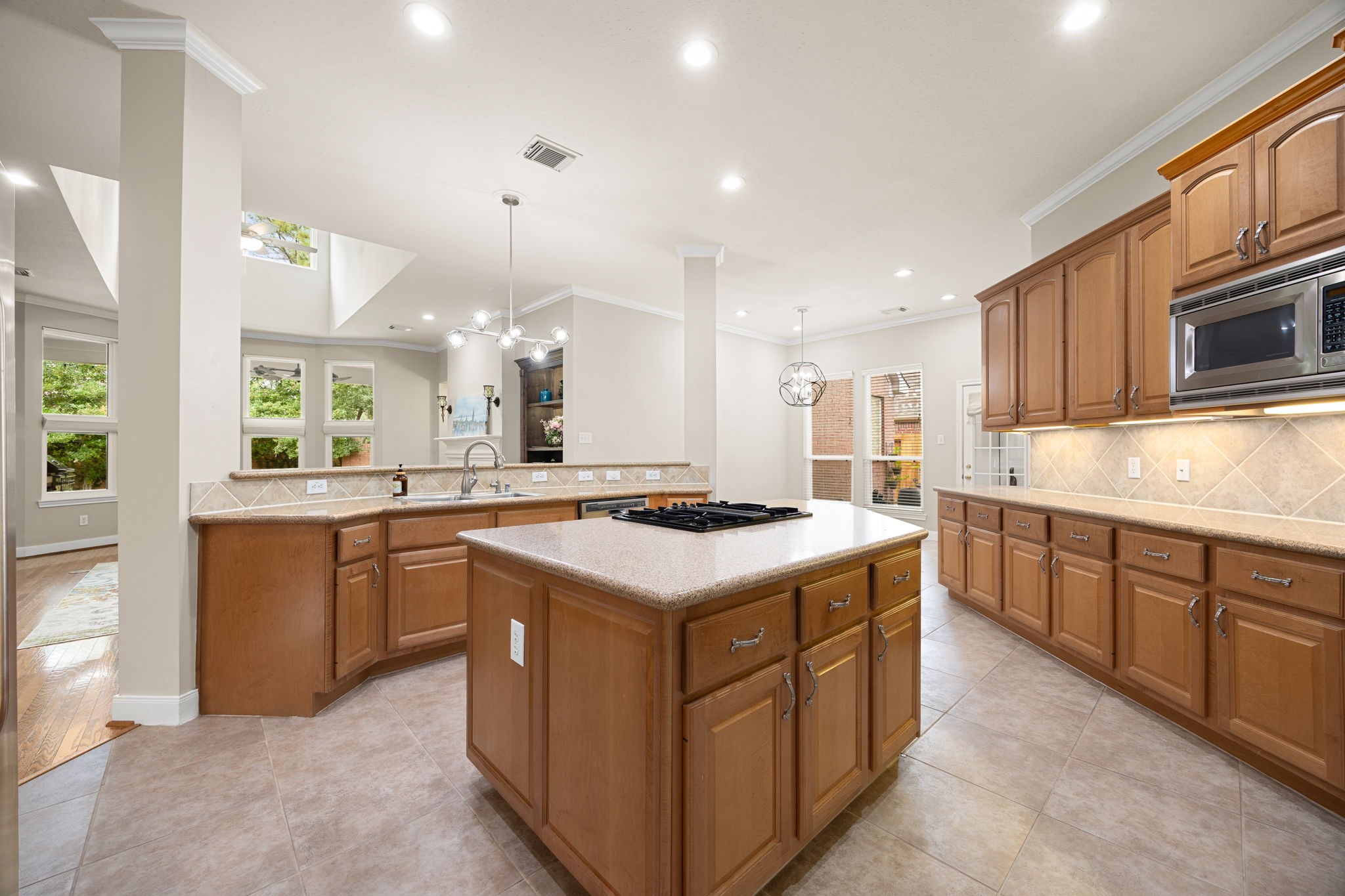 This perspective captures the endless counter space, sophisticated under-cabinet lighting, and an expansive breakfast bar flanking the kitchen. With views into the adjacent sunlit breakfast nook and main living areas, this layout blends functional work zones with a highly social, open-concept lifestyle.