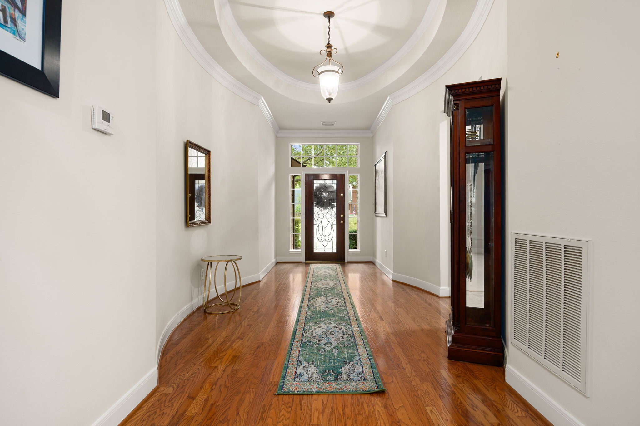 Step through the front door into a spectacular foyer featuring an elegant, curved architectural gallery layout. Rich, gleaming wood floors, soaring ceilings with custom tray detailing, and a classic statement light fixture seamlessly guide you toward the heart of the home. Step through the front door into a spectacular foyer featuring an elegant, curved architectural gallery layout. Rich, gleaming wood floors, soaring ceilings with custom tray detailing, and a classic statement light fixture seamlessly guide you toward the heart of the home.