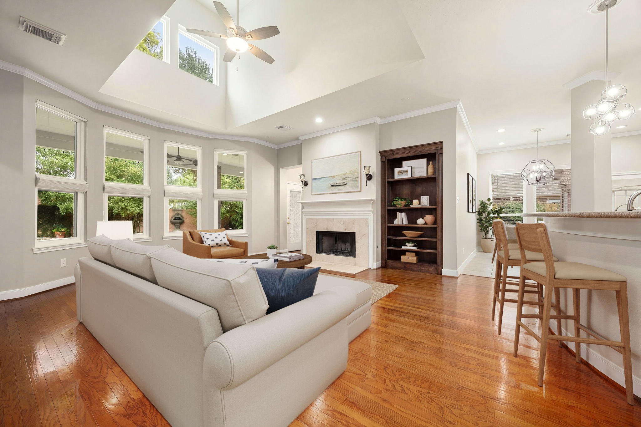 Sun-drenched and spacious, the family room is the heart of this open-concept layout. High, vaulted architectural ceilings and a towering wall of windows fill the space with beautiful natural light. Gleaming hardwood floors lead to a cozy fireplace flanked by beautiful custom dark-wood built-ins, with a seamless view into the adjacent kitchen and bar area. Sun-drenched and spacious, the family room is the heart of this open-concept layout. High, vaulted architectural ceilings and a towering wall of windows fill the space with beautiful natural light. Gleaming hardwood floors lead to a cozy fireplace flanked by beautiful custom dark-wood built-ins, with a seamless view into the adjacent kitchen and bar area.