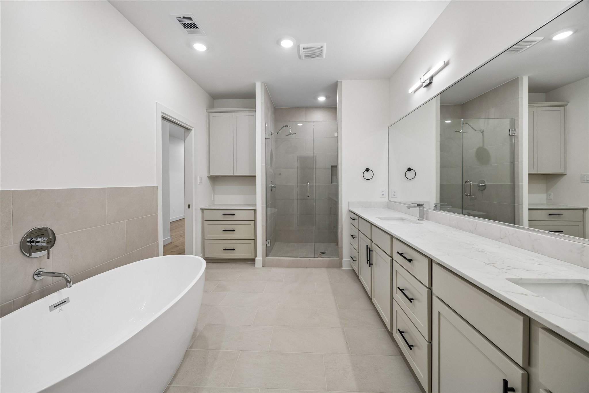 Luxurious primary bathroom featuring a freestanding soaking tub, glass-enclosed shower, dual vanities, and a dedicated counter area perfect for a morning coffee station.
