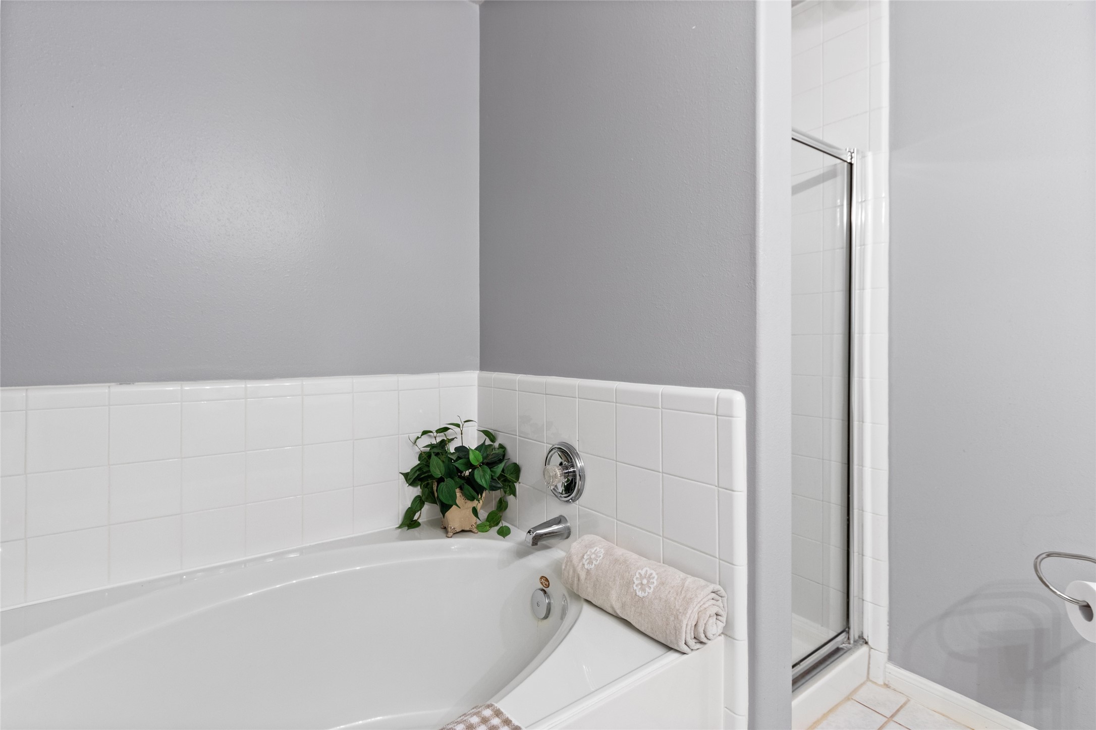 A stylish bathroom features a spacious bathtub with elegant white tile surround and a separate shower, accented by a soothing gray wall for a relaxing ambiance.