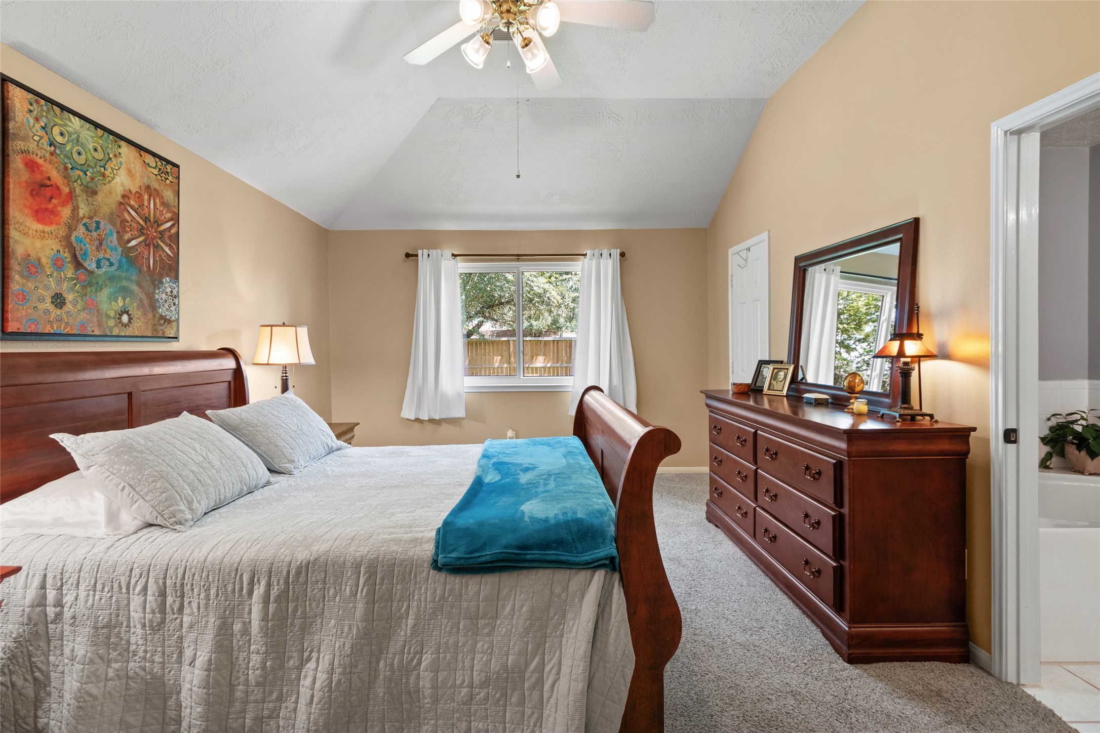 Spacious primary bedroom with a vaulted ceiling, ceiling fan, comfy carpet, and a large window offering plenty of natural light.