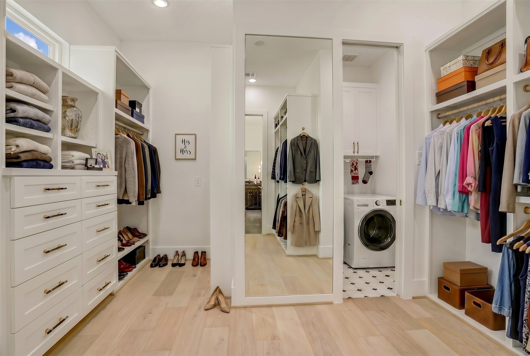 The primary closet, complete with built-ins and a full-length mirror, also allows for direct access to the utility room. Virtually staged photo.