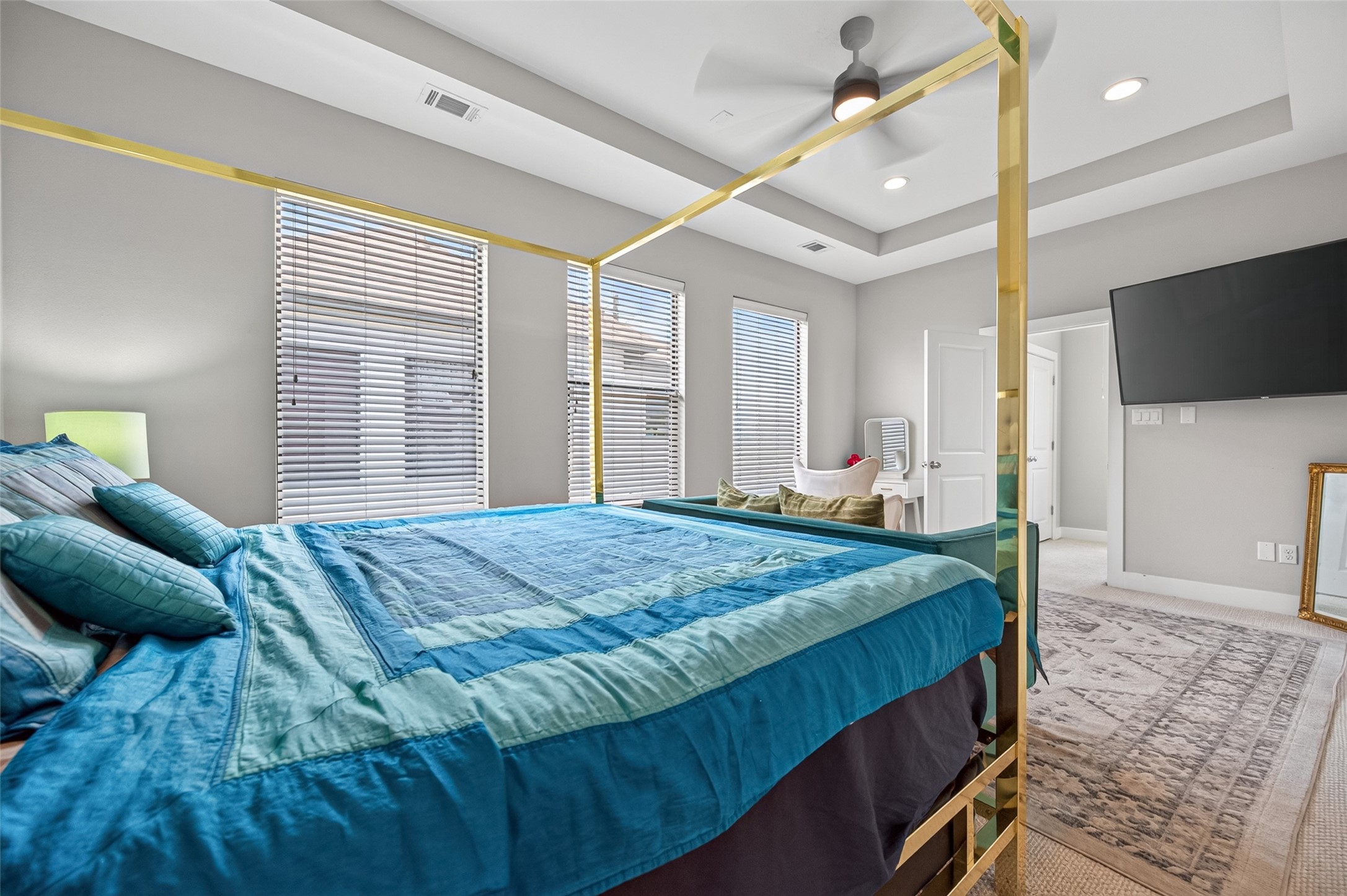 Spacious bedroom featuring a luxurious canopy bed, modern ceiling fan, and large windows for ample natural light, complemented by a sleek wall-mounted TV and cozy seating area.