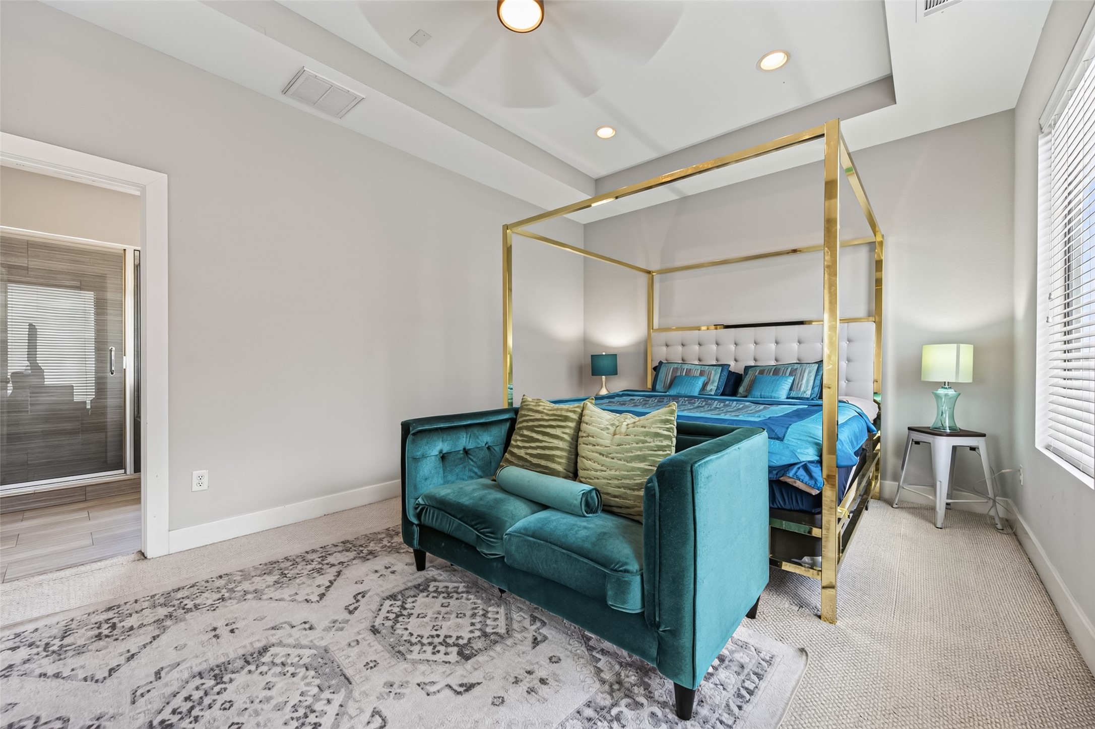 Spacious bedroom featuring a luxurious canopy bed, modern ceiling fan, and ample natural light from large windows, complemented by a cozy seating area and stylish decor.