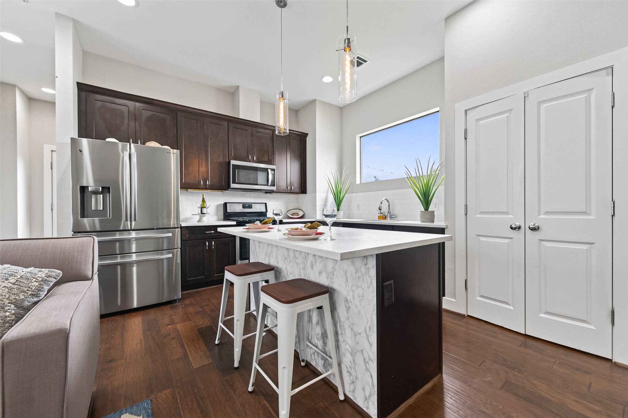 Modern open-concept living area with sleek kitchen, featuring stainless steel appliances, a large island with bar seating, and rich hardwood floors, complemented by a cozy seating area and plenty of natural light.