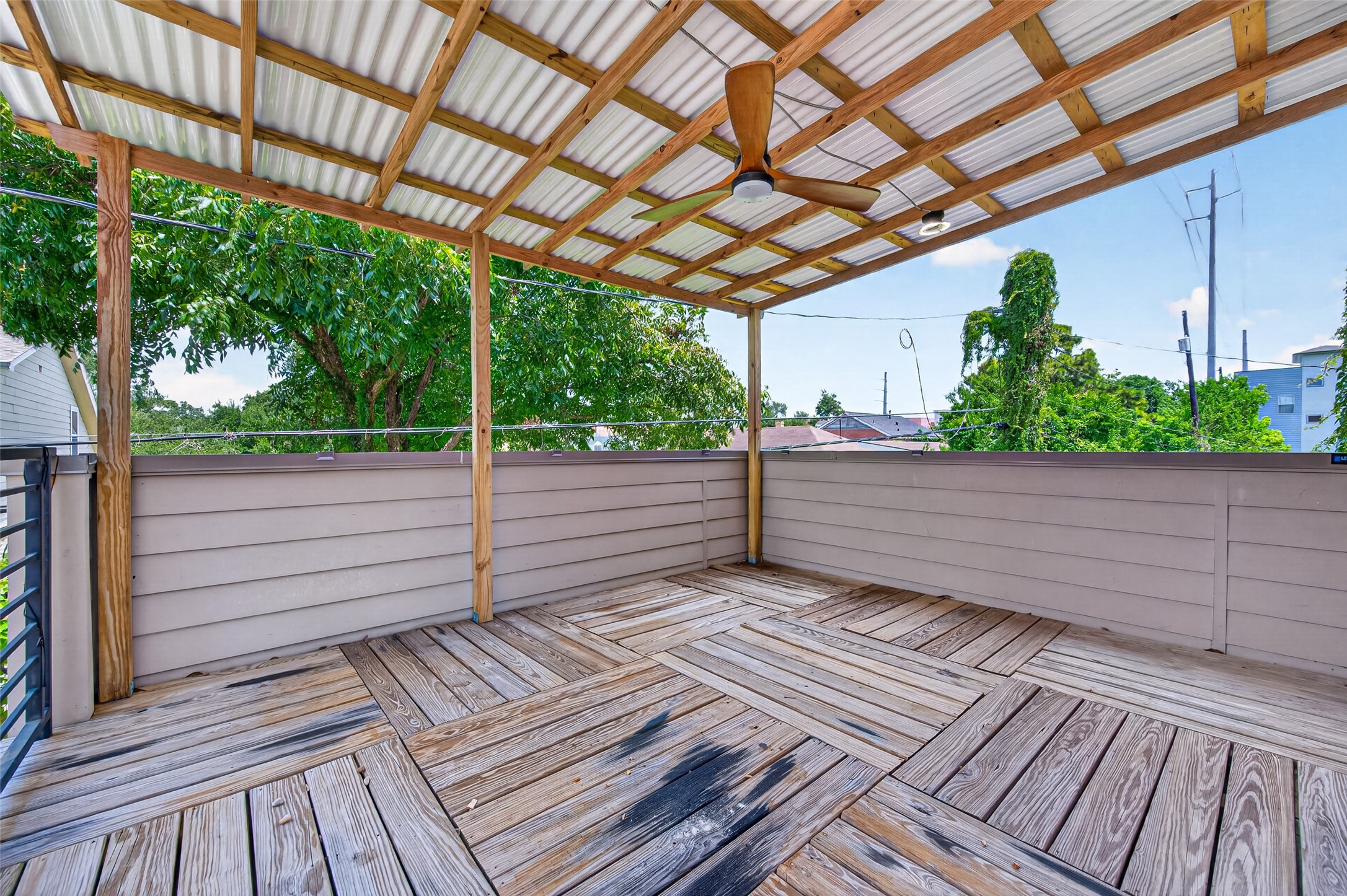 Spacious covered deck with a stylish wood pattern, perfect for outdoor relaxation and entertaining, featuring a ceiling fan for comfort.