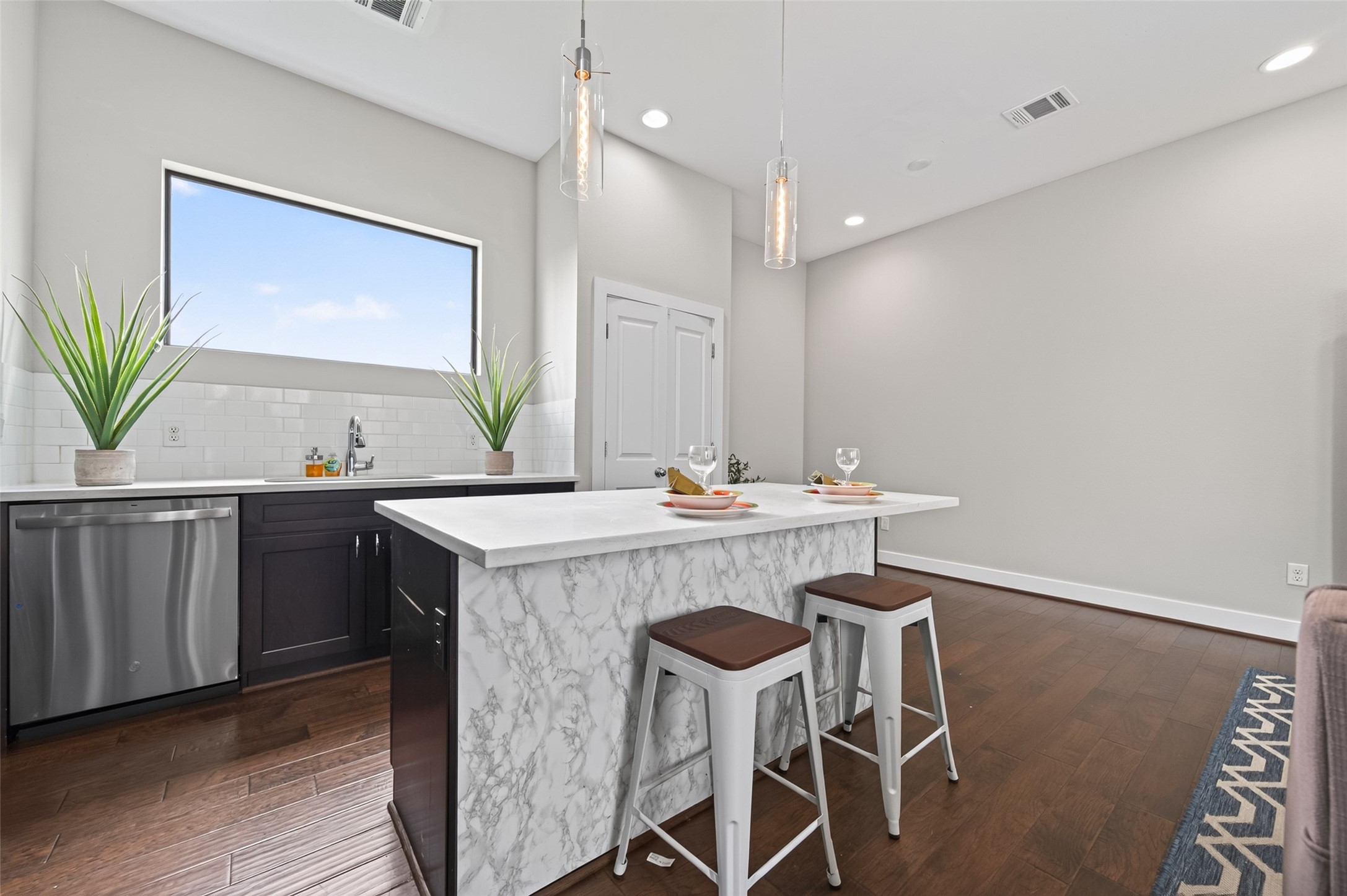 Modern open-concept living area featuring sleek hardwood floors, a central island with dark cabinetry, and ample natural light from large windows.