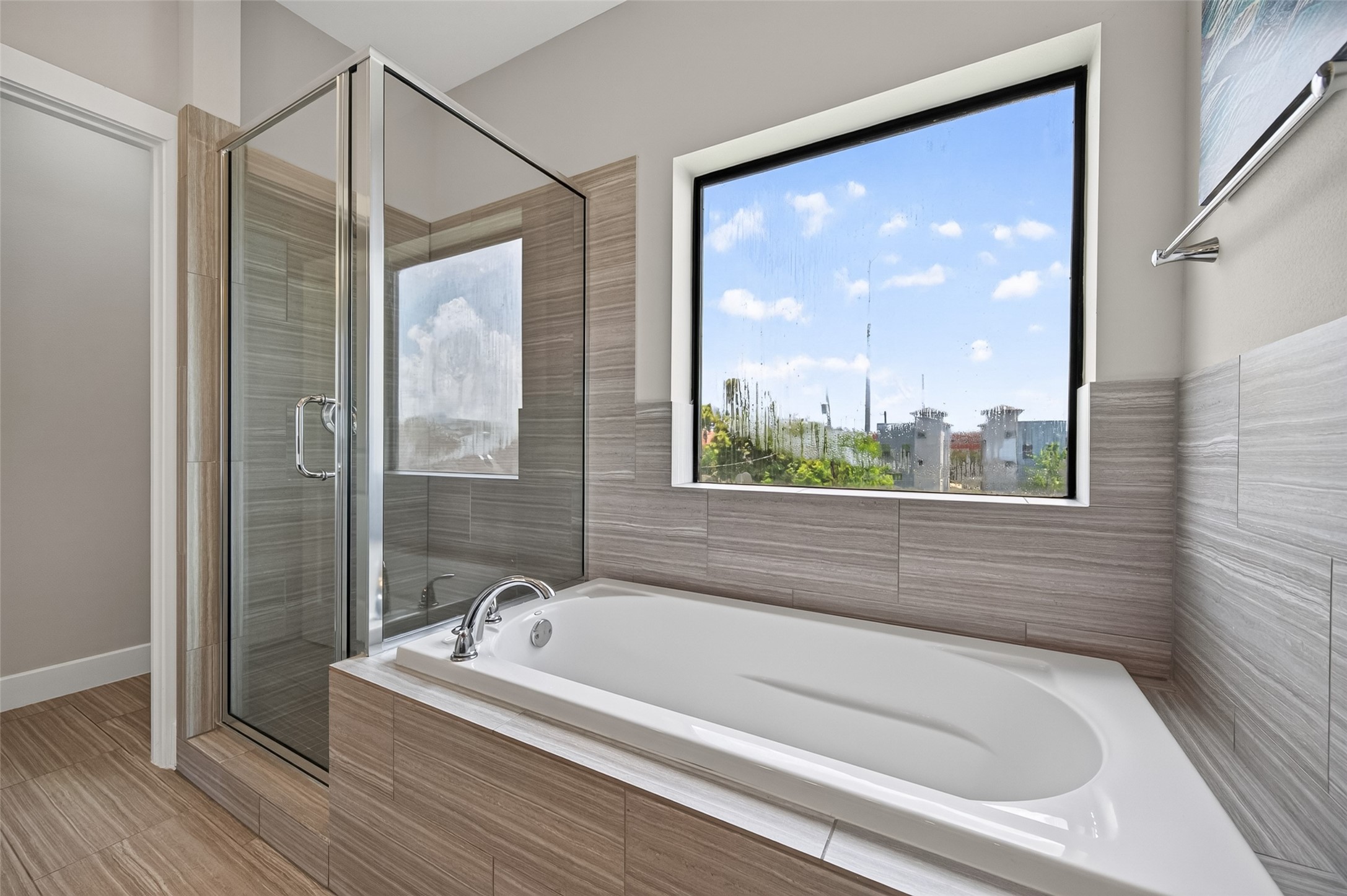 Elegant bathroom featuring a modern soaking tub with sleek fixtures, complemented by stylish tilework and a large window offering natural light and pleasant views.