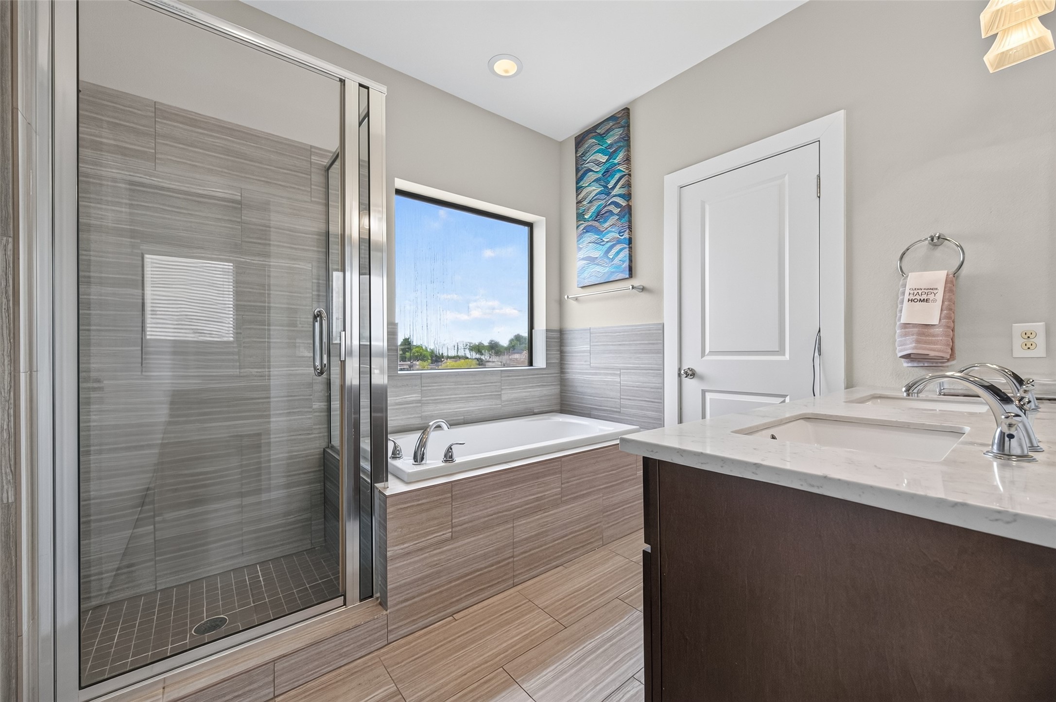 Modern bathroom featuring a spacious glass-enclosed shower, sleek soaking tub beneath a large window, and a stylish vanity with dual sinks, offering both elegance and functionality.