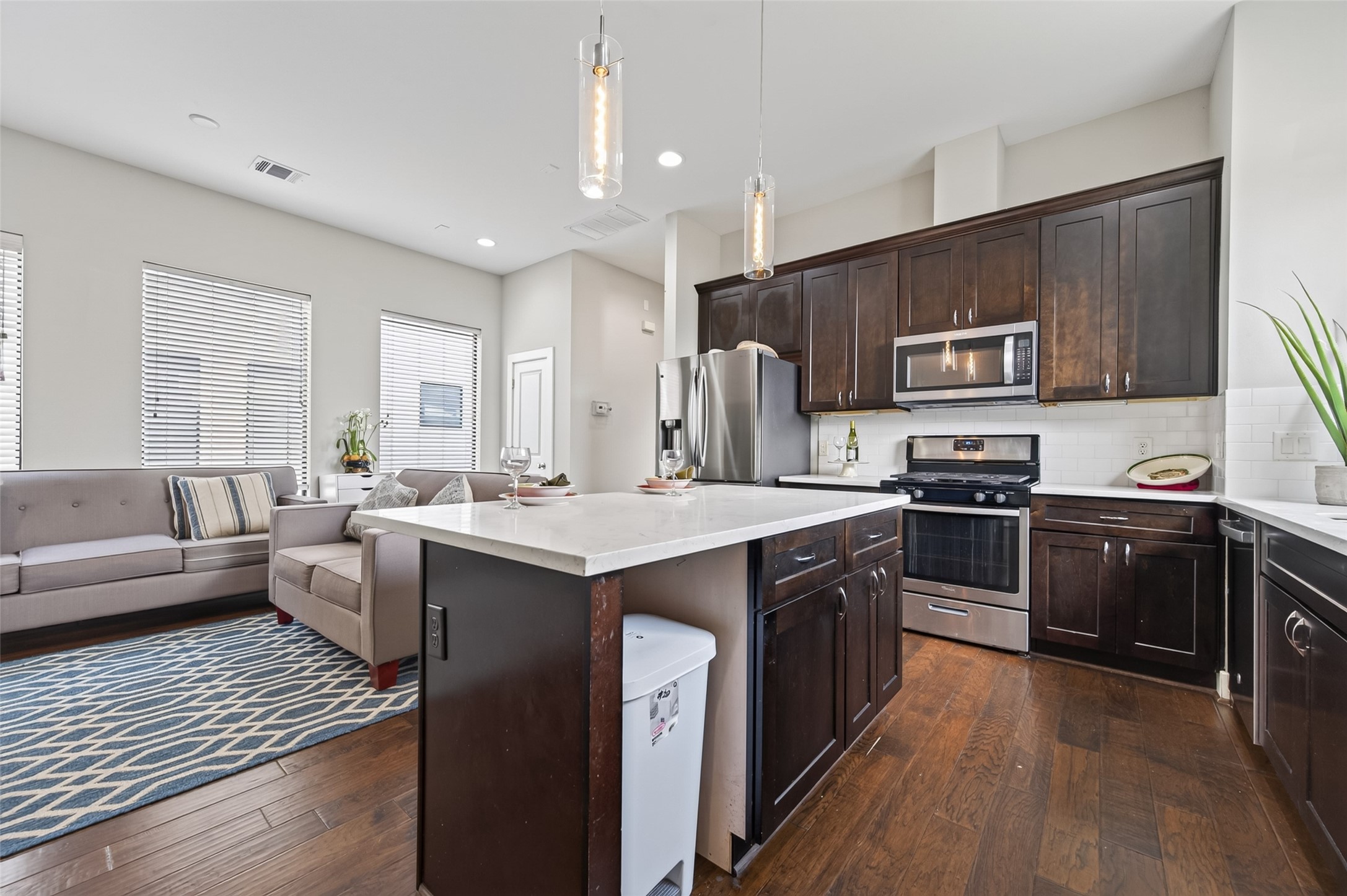 Modern kitchen with sleek stainless steel appliances, rich dark cabinetry, and a stylish marble island featuring seating for two. The space is accented by pendant lighting and a bright window, creating an inviting atmosphere.