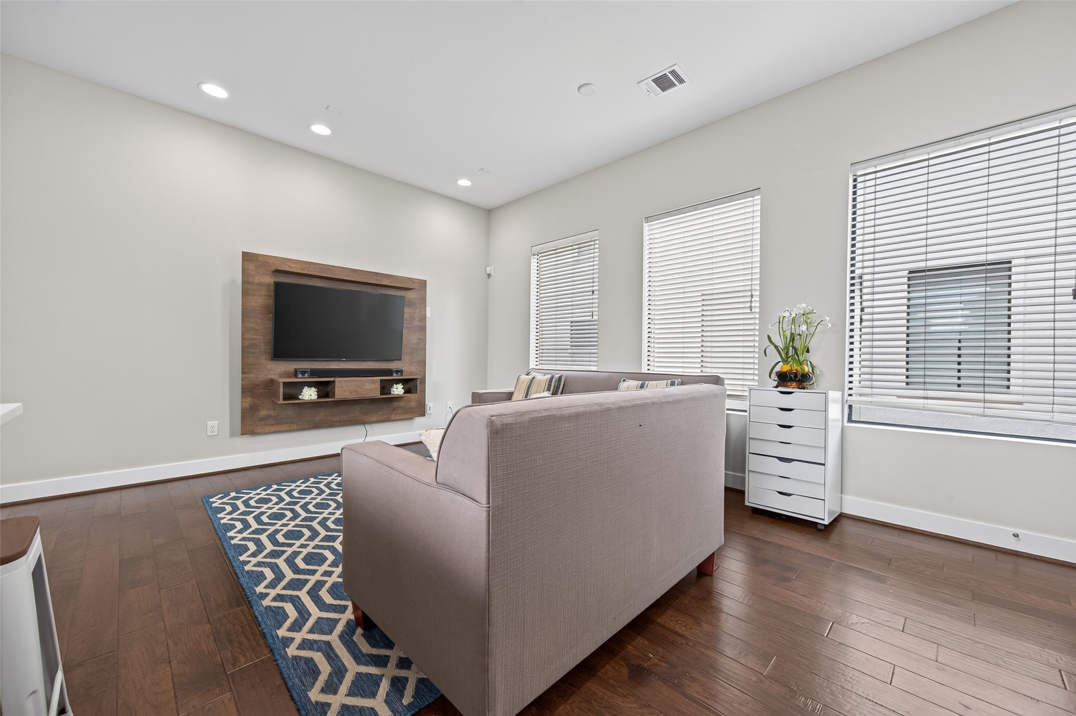 Bright and inviting open-concept living area featuring stylish sofas, a chic geometric rug, and a sleek, modern kitchen with stainless steel appliances.
