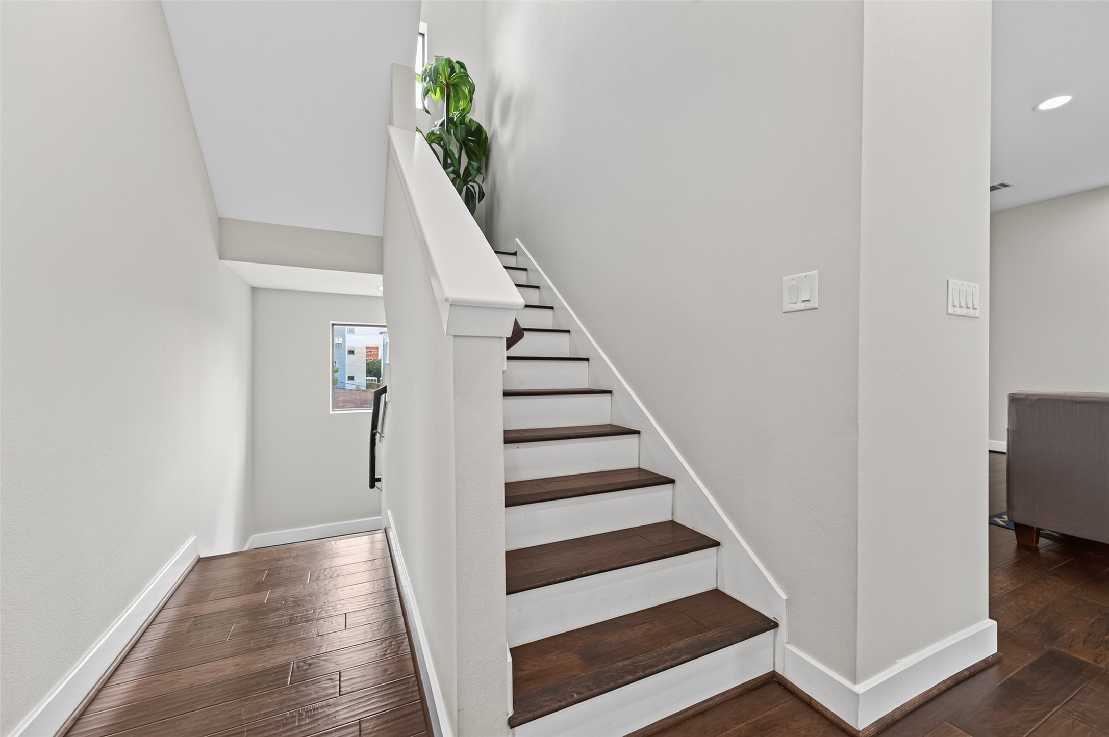 A modern staircase with rich wooden steps leads upward, complemented by crisp white walls and a sleek white door, creating a clean and inviting entryway.