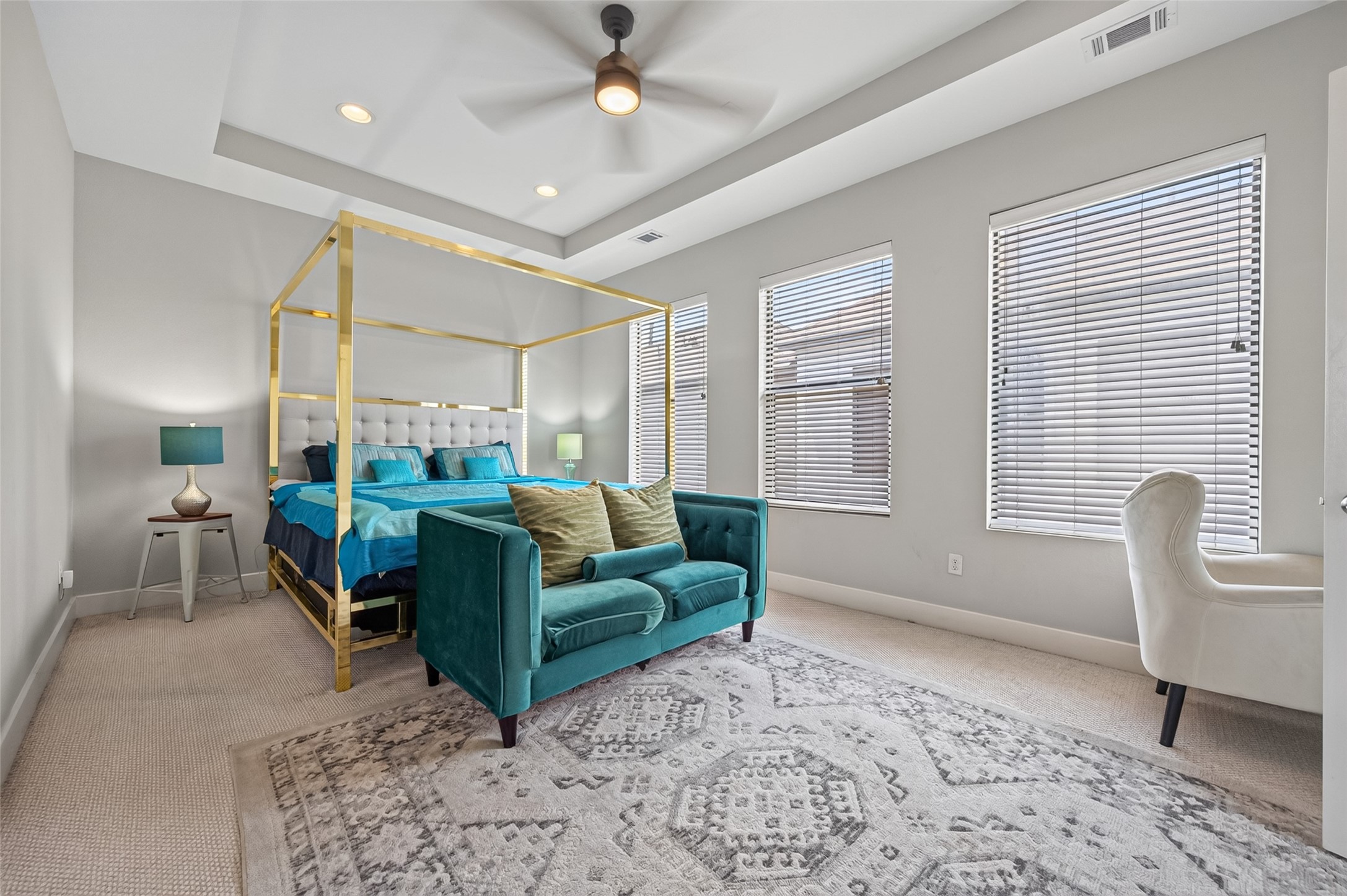 Spacious bedroom featuring a luxurious canopy bed with plush teal accents, complemented by a stylish area rug and abundant natural light.
