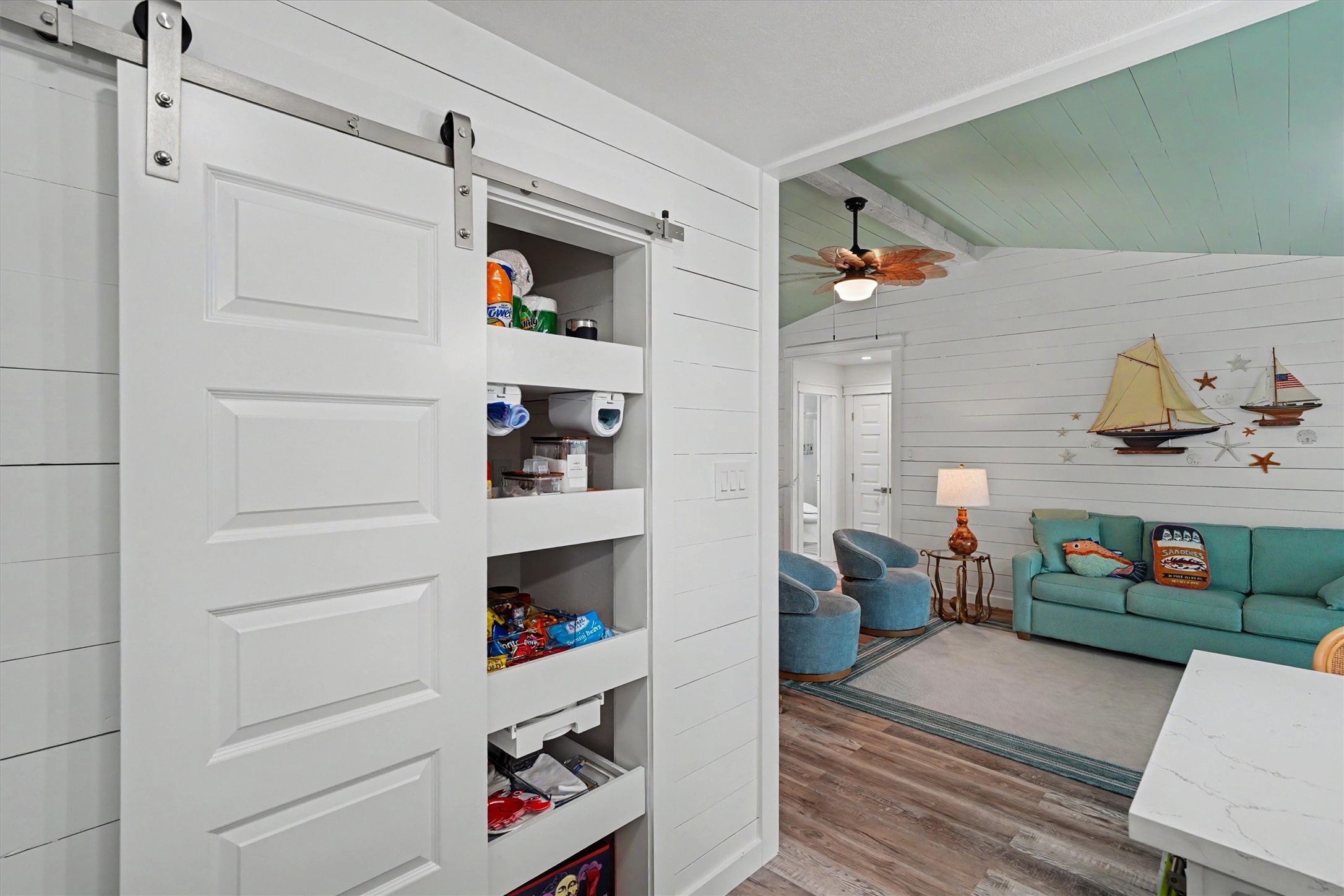 This inviting open-concept layout brings the kitchen and living spaces together beautifully. The updated kitchen maximizes every inch with a pantry featuring convenient pull-out shelving, while modern shiplap walls add texture, character, and a fresh coastal feel This inviting open-concept layout brings the kitchen and living spaces together beautifully. The updated kitchen maximizes every inch with a pantry featuring convenient pull-out shelving, while modern shiplap walls add texture, character, and a fresh coastal feel