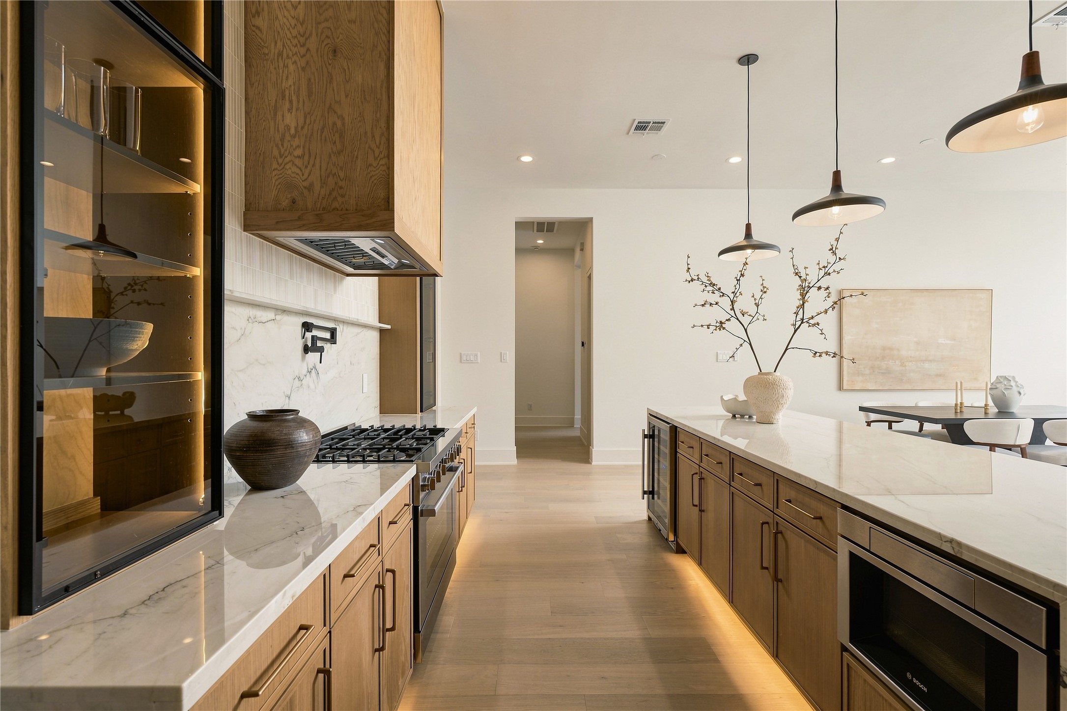 A dramatic perspective showcases the kitchens Midnight Glass Towers and illuminated cabinetry, creating a striking contrast against the warmth of the white oak finishes