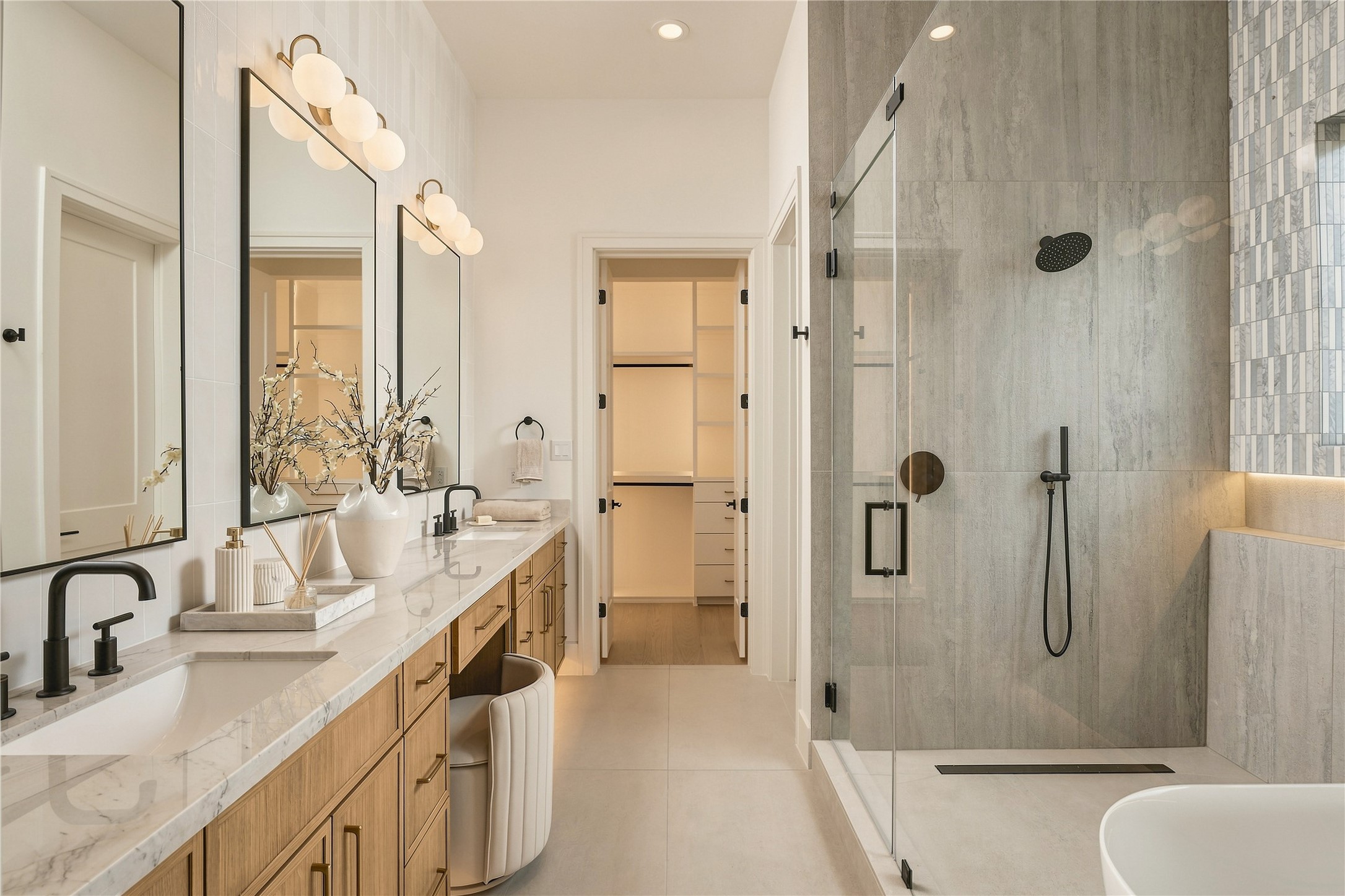 The primary bath delivers a spa-like experience with a generous dual vanity, dedicated makeup station, and an oversized frameless glass shower with a ceiling-mounted rainfall showerhead.