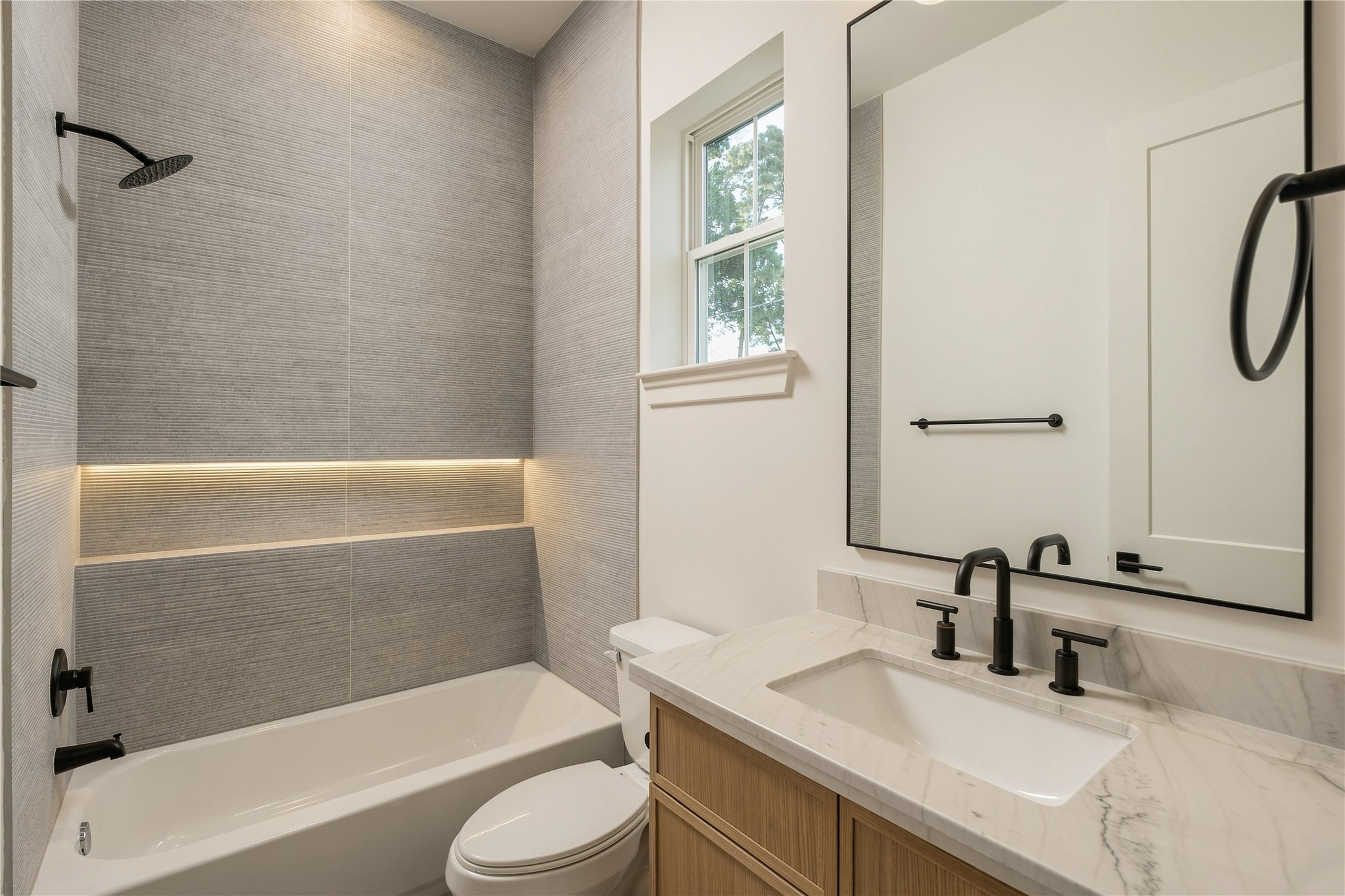 A well-appointed secondary bath features a frameless glass shower, full-height designer tile, and an illuminated shower niche, continuing the homes attention to detail across every ensuite.
