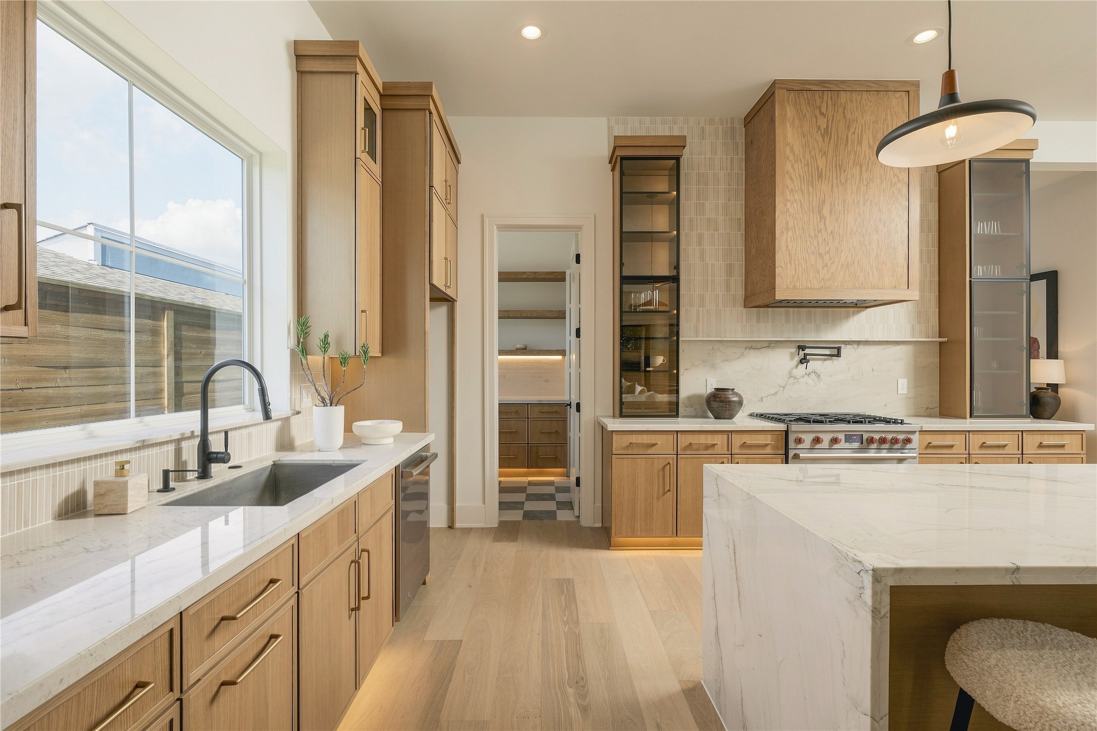 A closer view reveals the kitchens layered craftsmanship, where custom white oak details, glass-front cabinetry, and integrated LED lighting bring warmth and dimension to the space.
