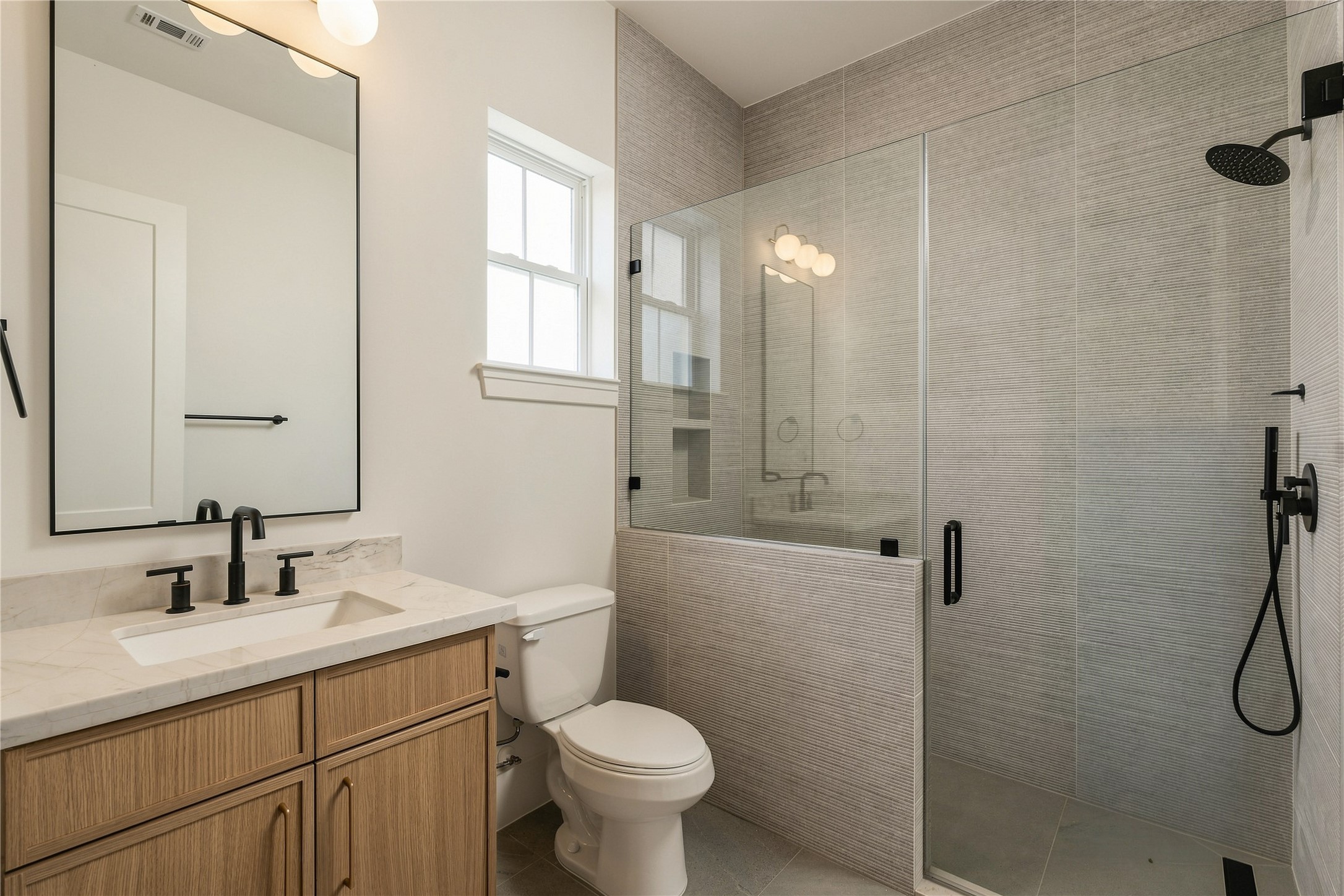This secondary bath pairs Mount Blanc Quartzite with full-height designer tile and a frameless glass shower, creating a polished ensuite experience with finishes typically reserved for a primary suite.