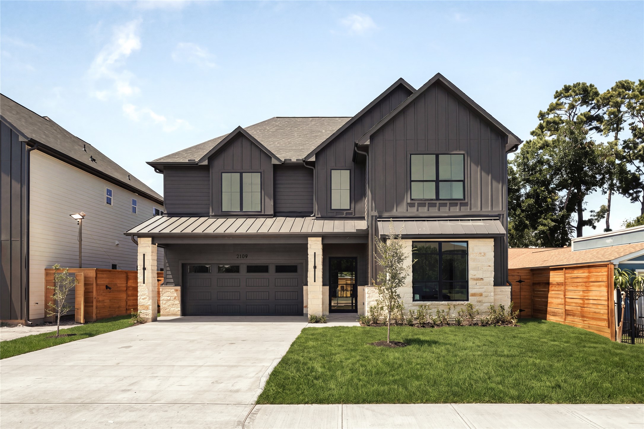A commanding street presence introduces the home with limestone accents, custom wood detailing, and an 18-foot glass-panel garage door, balancing modern architecture with warm, natural materials.