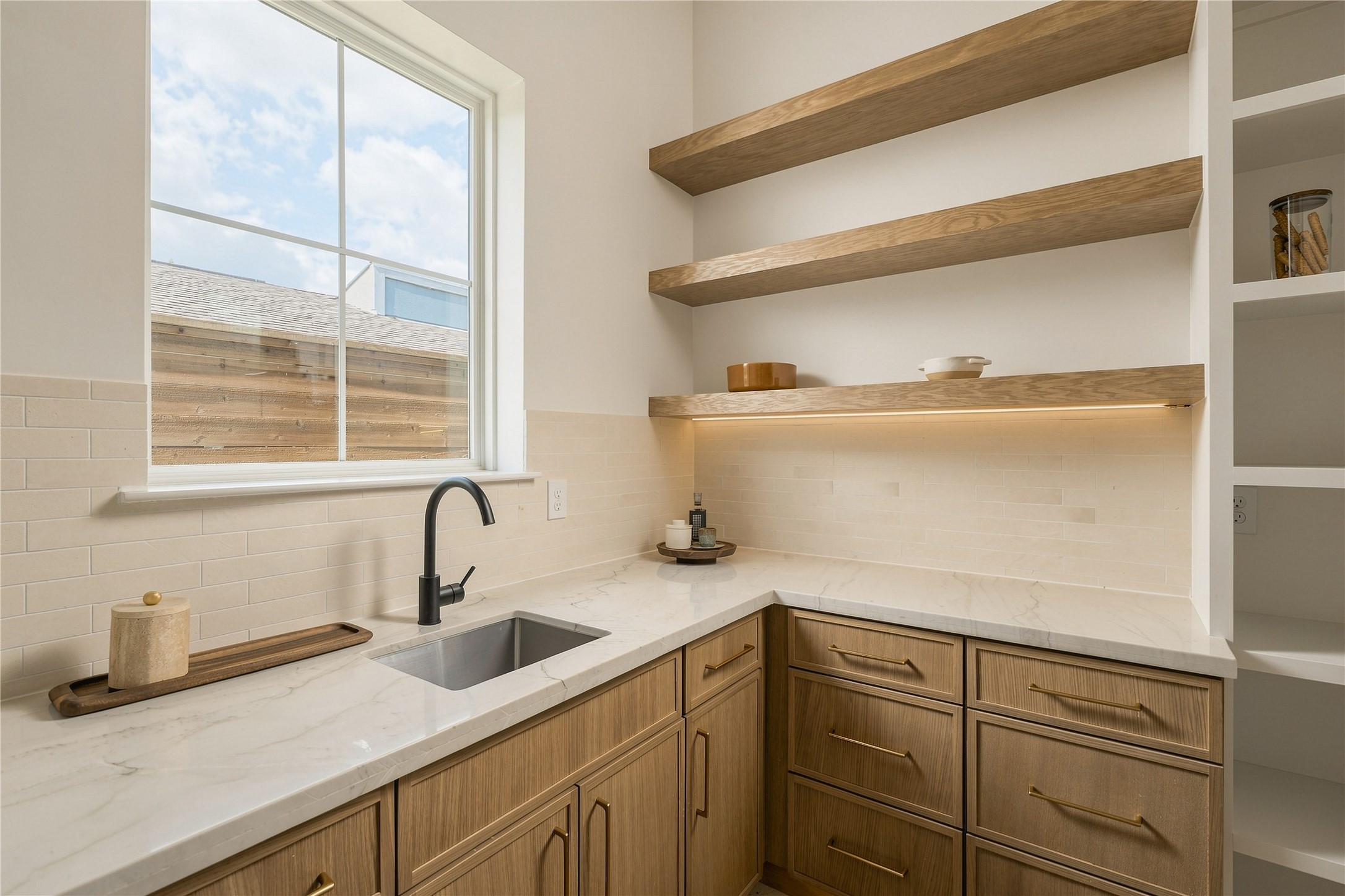 A discreet scullery-style pantry extends the kitchens functionality with generous prep space, additional cabinetry, open white oak shelving, and its own sinkkeeping the main kitchen ready for entertaining.