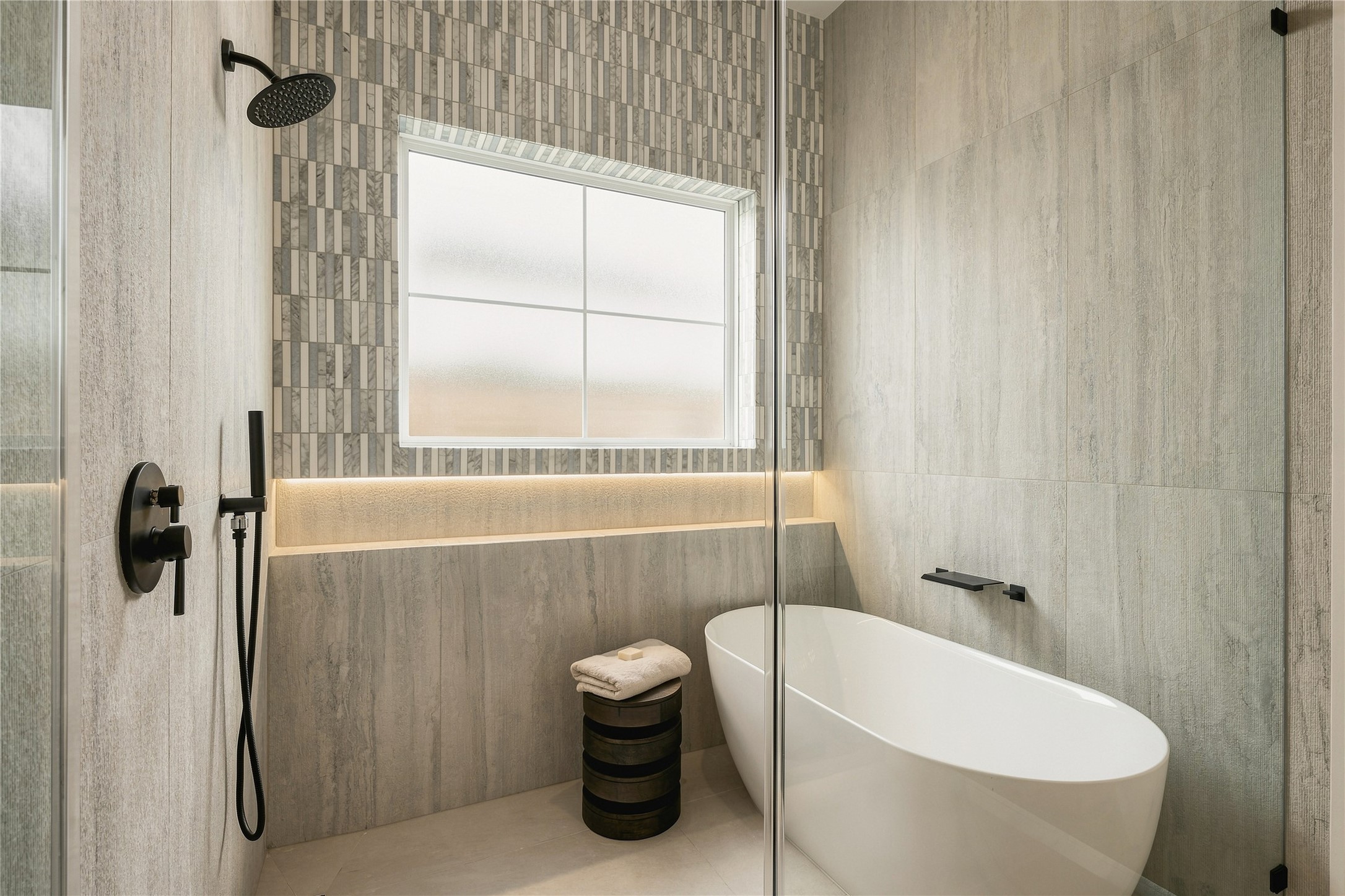 A private water closet is finished with full-height designer tile and natural light, carrying the primary baths refined material palette through every detail.